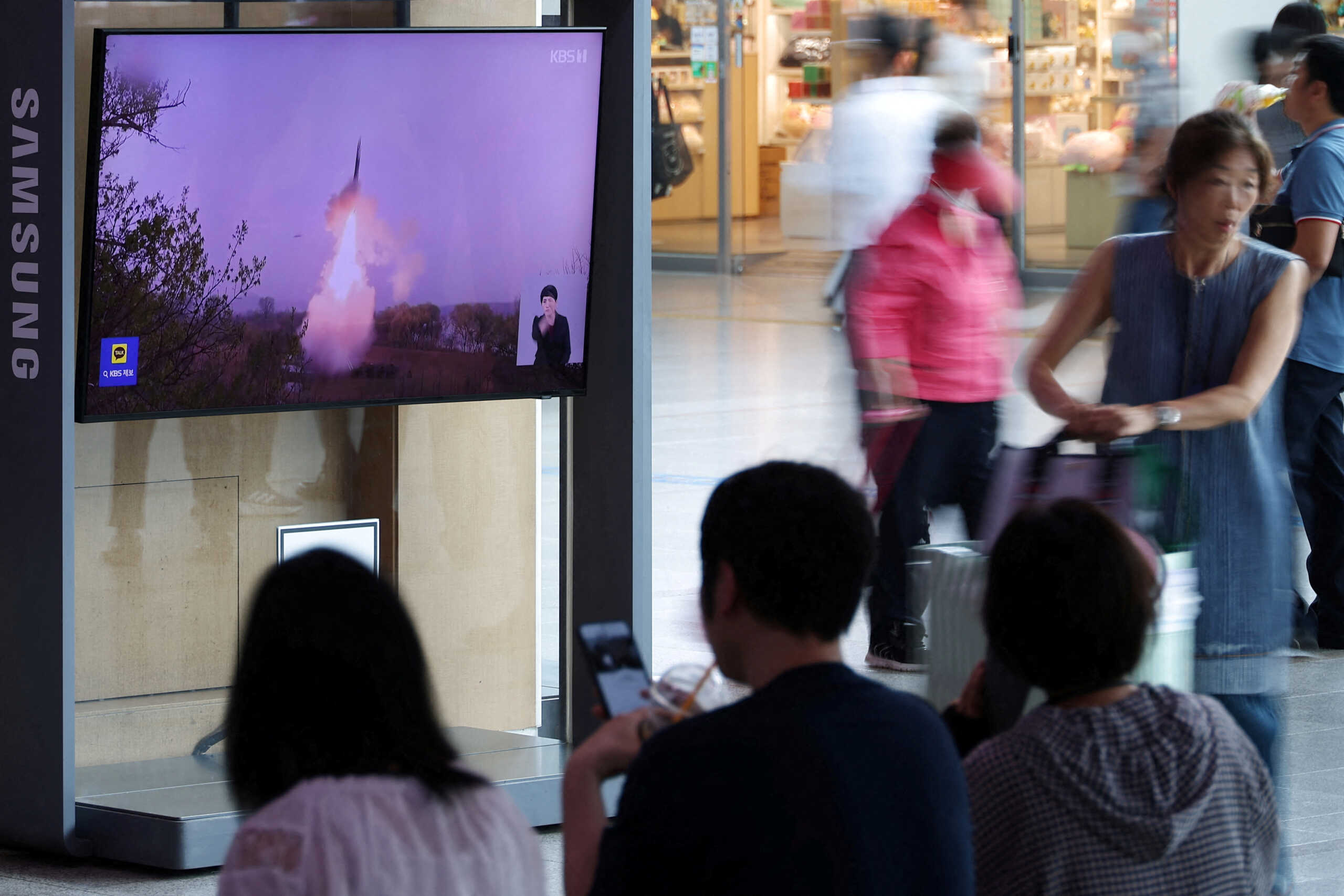 FILE PHOTO: Passengers wait for their train in front of a TV broadcasting a news report on North Korea firing a ballistic missile off its east coast, at a railway station in Seoul, South Korea, July 12, 2023.    REUTERS