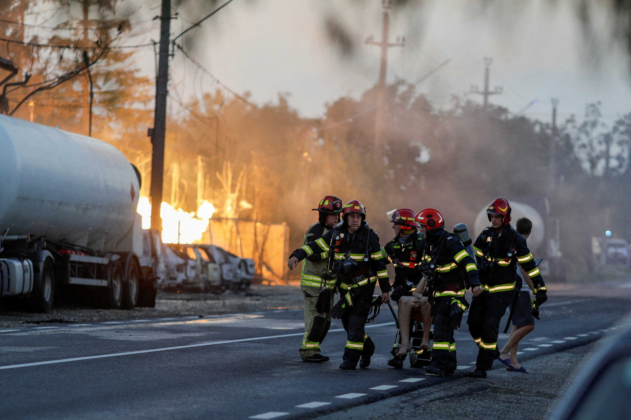 Firefighters carry a person as flames rise after an explosion at a LPG station in Crevedia, near Bucharest, Romania, August 26, 2023. Inquam Photos