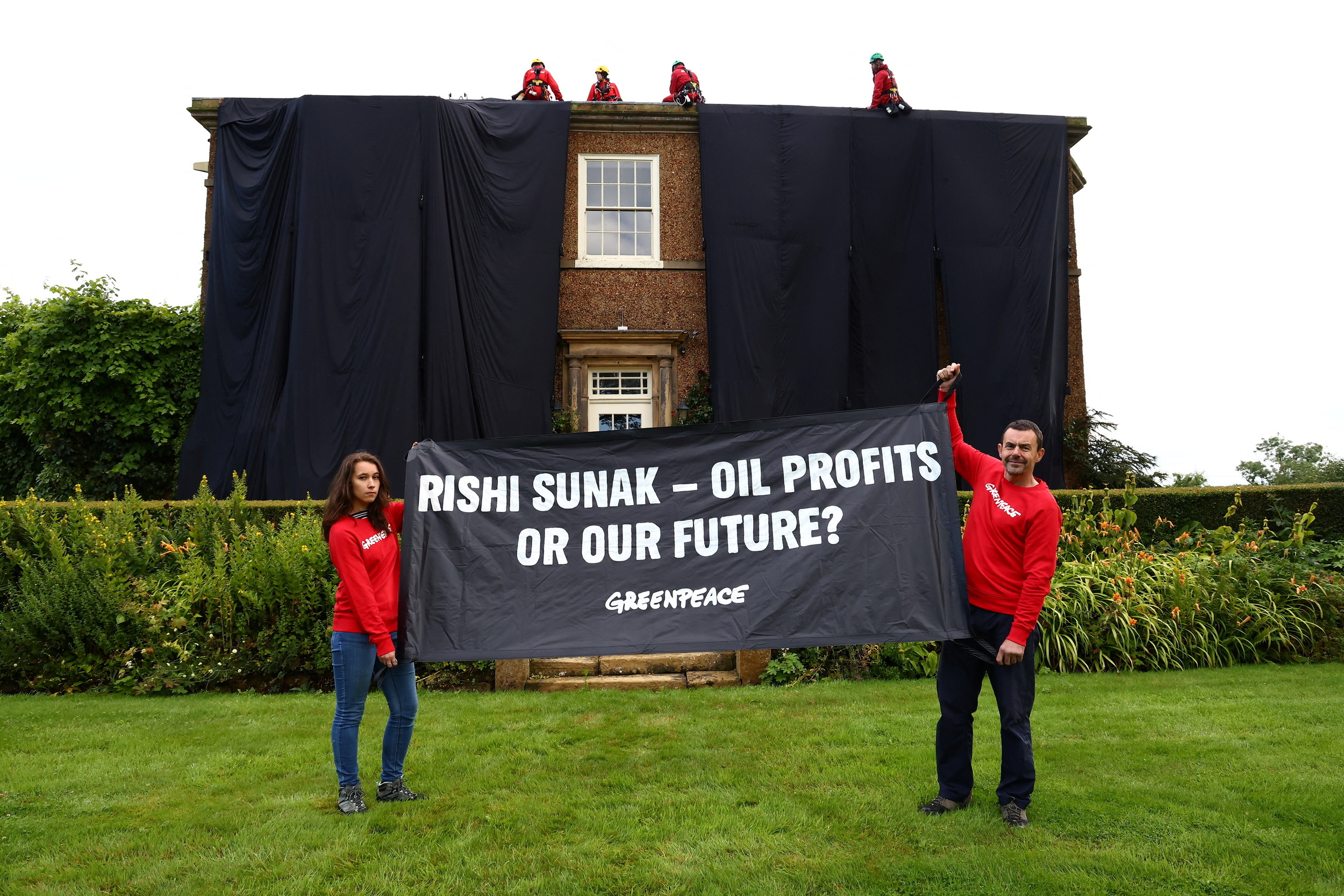 Greenpeace activists hold a banner while others cover British Prime Minister Rishi Sunak's £2m manor house in oil-black fabric in protest of his backing for a major expansion of North Sea oil and gas drilling amidst a summer of escalating climate impacts, in Yorkshire, Britain August 3, 2023. Greenpeace