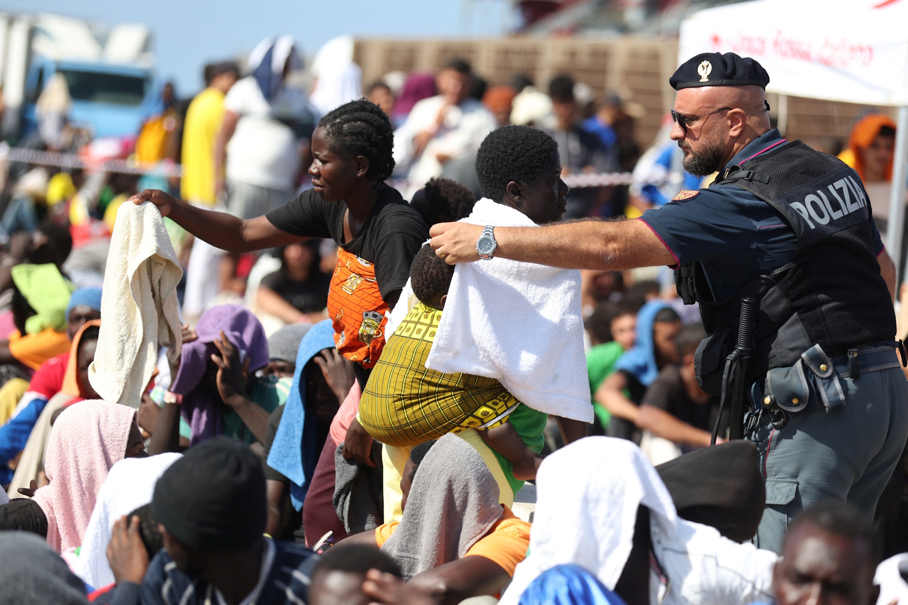 A policeman covers a baby with a towel as migrants wait at the port to be transferred to the mainland, on the Sicilian island of Lampedusa, Italy, September 15, 2023. REUTERS