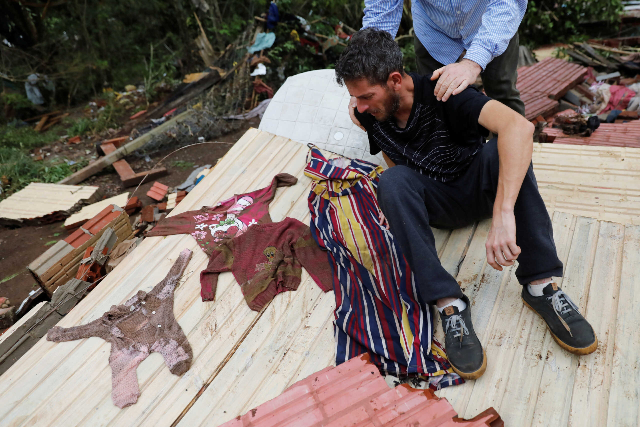 Flood survivor Miguel Rutigliano Bieleski is comforted on the wreckage of his house, as he gets emotional after finding clothes of his wife Ariel Armani, his daughter Yasmin and his son Miguel Junior, that are still missing, after the passage of the extratropical cyclone that hit the region, Lajeado, Brazil September 8, 2023. REUTERS