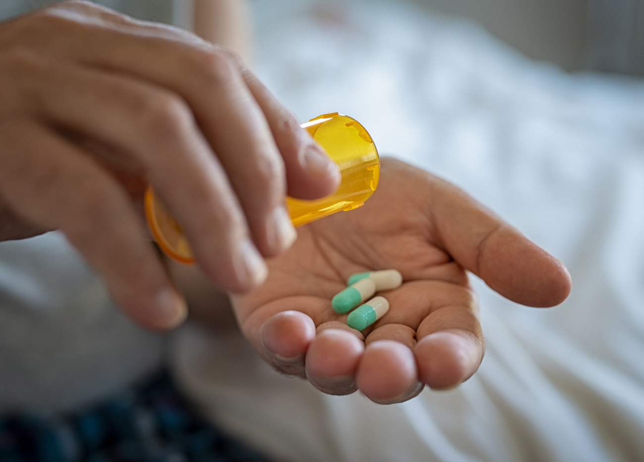 Closeup of man hand pouring capsules from a pill bottle into hand. Senior man taking daily medicine to consume. Close up of male hands taking daily dose of drug.