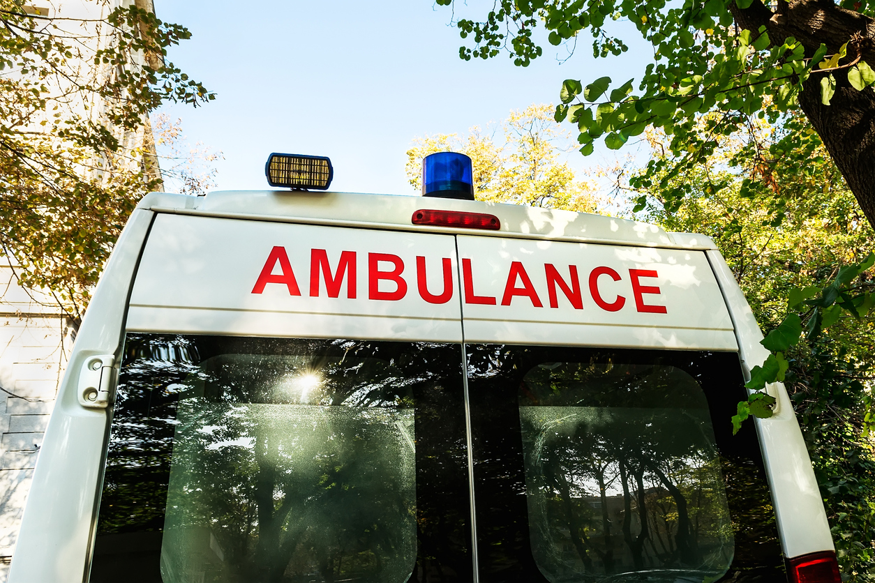 Stationary white ambulance car with a blue warning light on a roof. An emergency medical service van. On a sunny autumn day. Rear view.