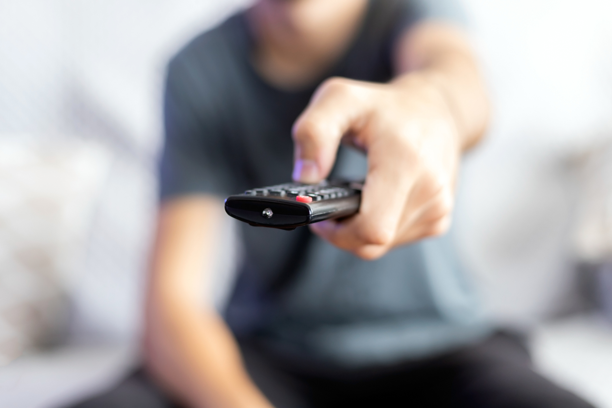 A man sitting on a sofa changes the channel with a remote control. selective focus