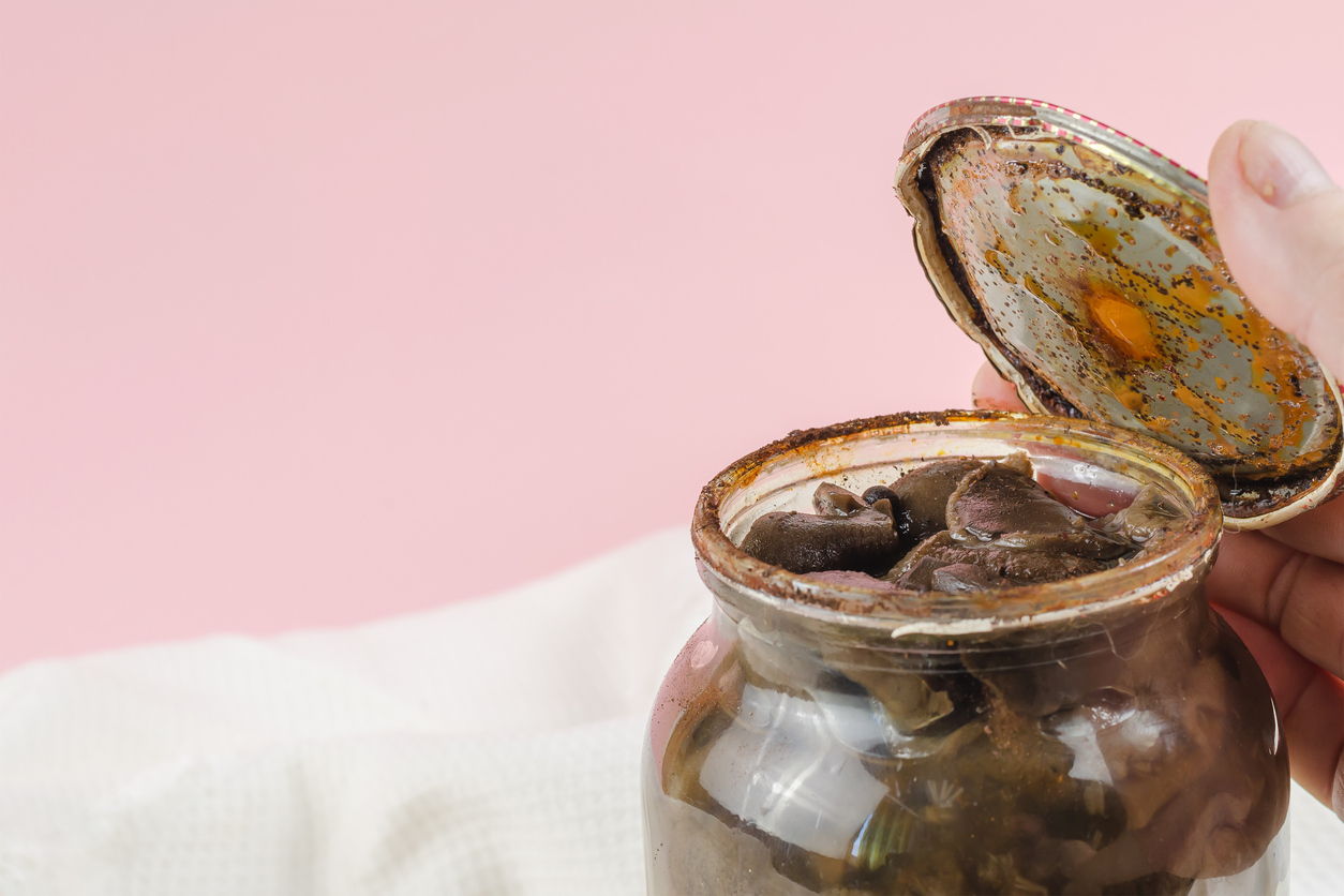 Botulism, food poisoning from canned foods concept. Handholds Rusty tin lid with black stains. Opened Glass jar with homemade pickled Suillus. Spoiled blackened forest mushrooms
