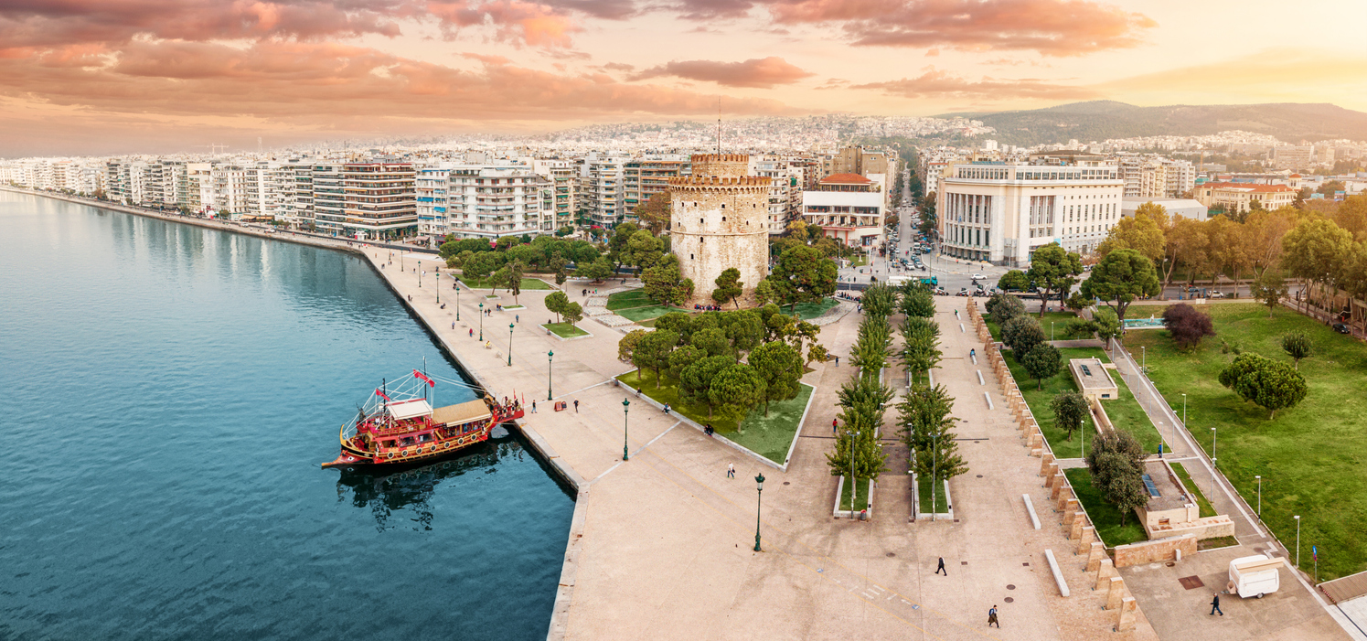 Aerial panoramic view of the main symbol of Thessaloniki city - the White Tower with boat tour ship at the pier. Concept of travel landmarks in Greece and urban development.