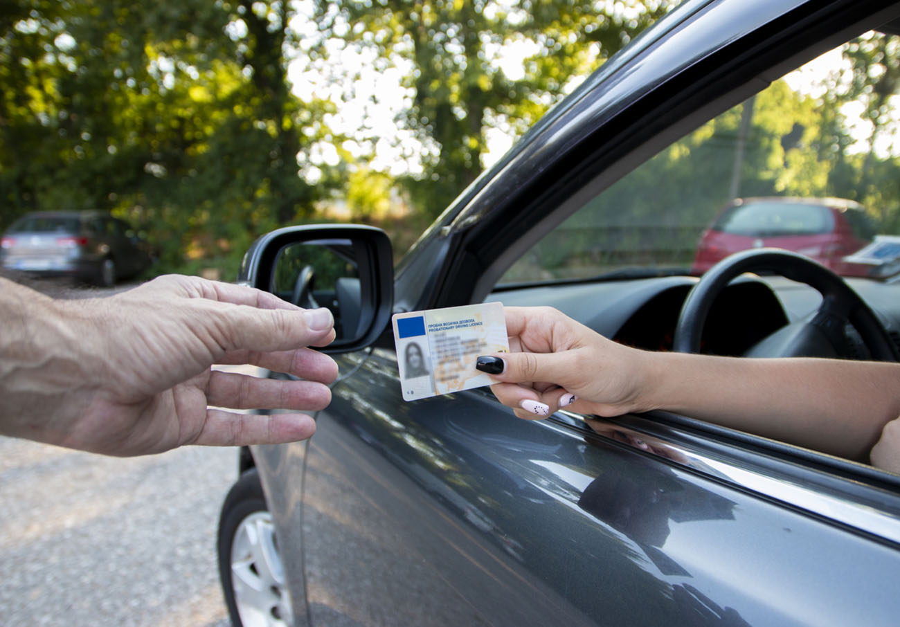 Teenager driver commited a minor offence and handing over her licence to a police officer reaching towards the open window.Police officer controlling traffic on the road