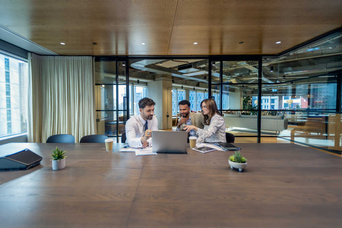 Business colleagues in a meeting, or Financial advisor or lawyer with couple explaining options. The agent is using a computer. All are well dressed. They sitting in an office meeting room. They are looking quite serious
