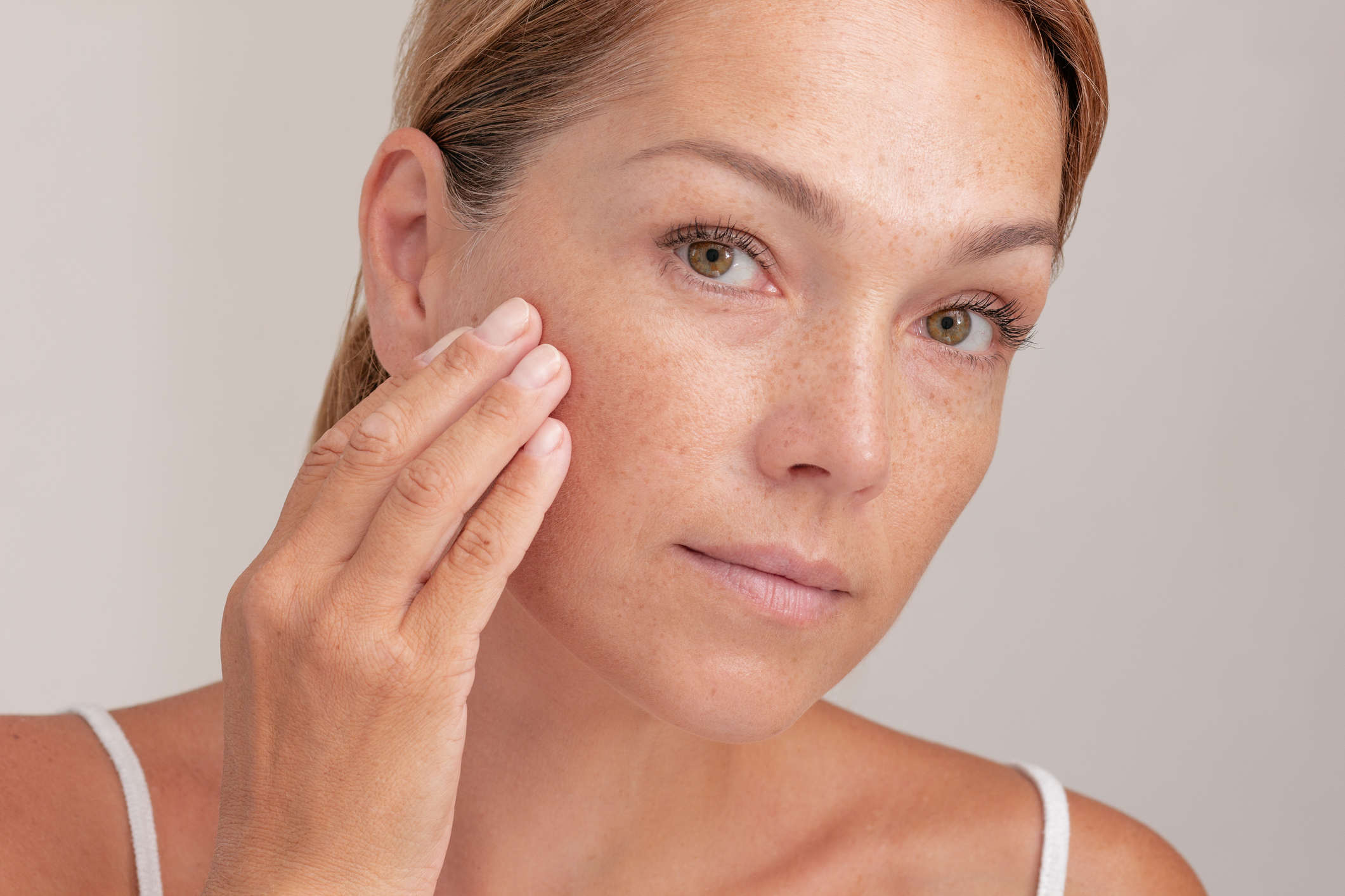 Portrait of cropped caucasian middle aged woman face with freckles touching skin by hand on white background