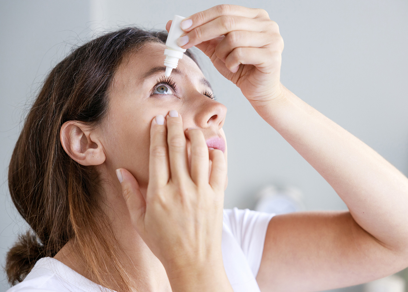 Young woman putting eye drops at home