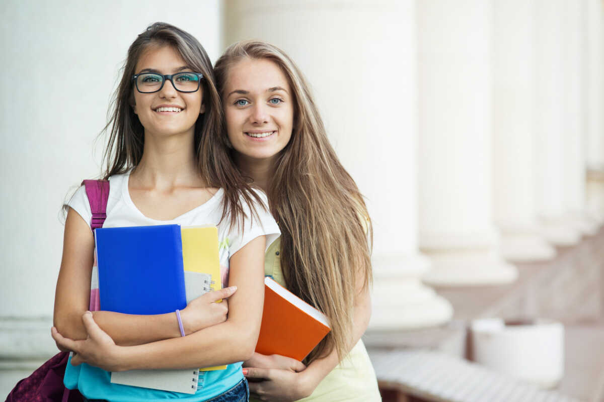 Schoolgirls holding textbooks and posing in front of the school.