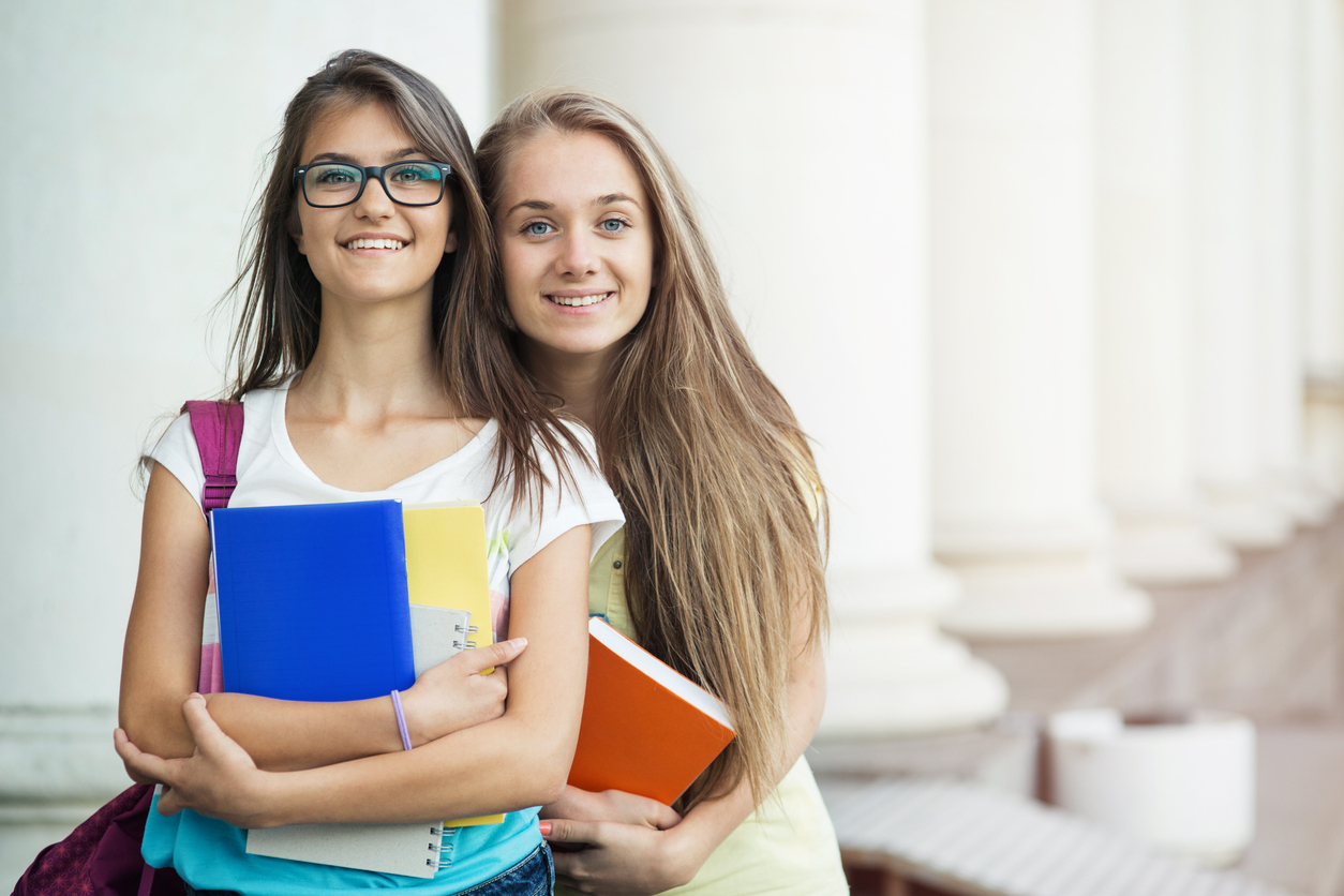 Schoolgirls holding textbooks and posing in front of the school.