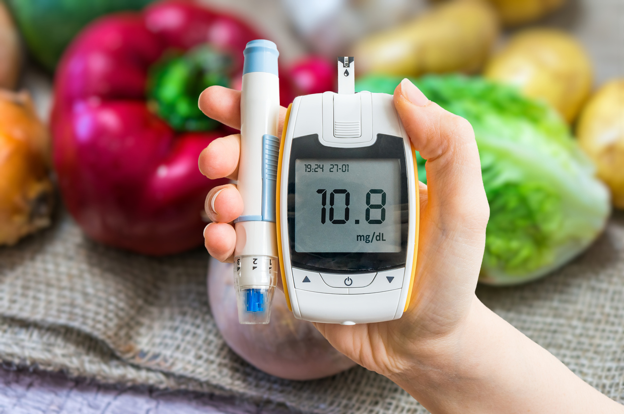 Diabetic diet and diabetes concept. Hand holds glucometer. Vegetables in background.