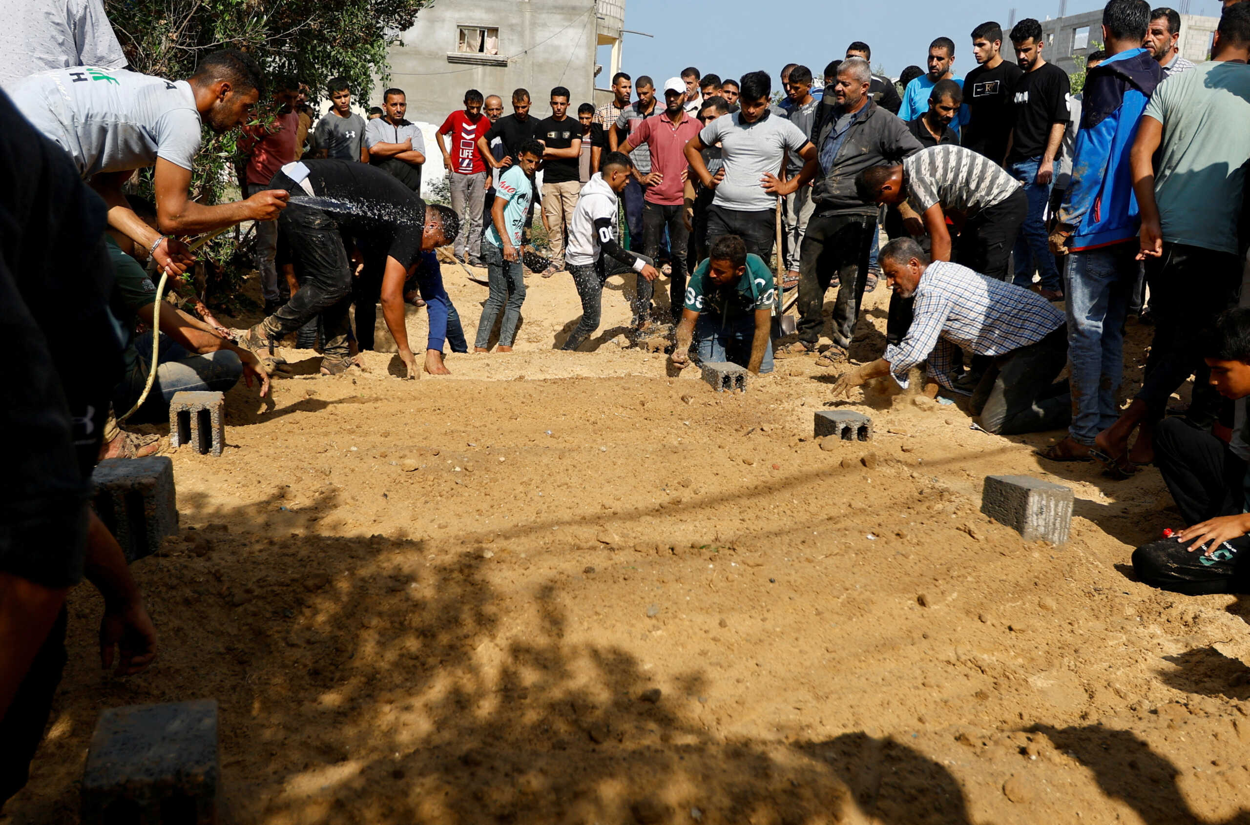 People sprinkle water on the graves after burying bodies of Palestinians from Samour family, who were killed in Israeli strikes on their house, at a land near to their home as the residents struggle to find spaces in cemeteries, in Khan Younis in the southern Gaza Strip October 12, 2023. REUTERS