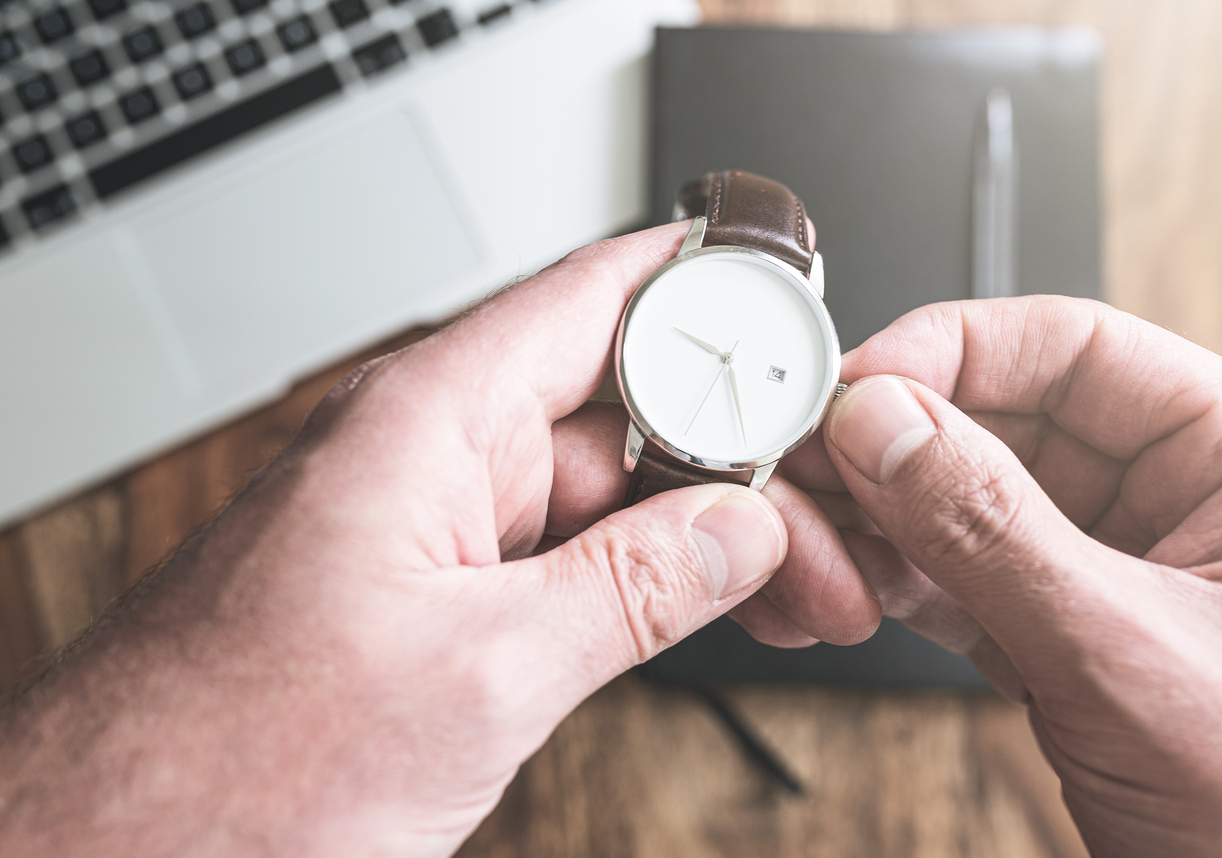 man setting his wristwatch against laptop computer and personal organizer on wooden desk