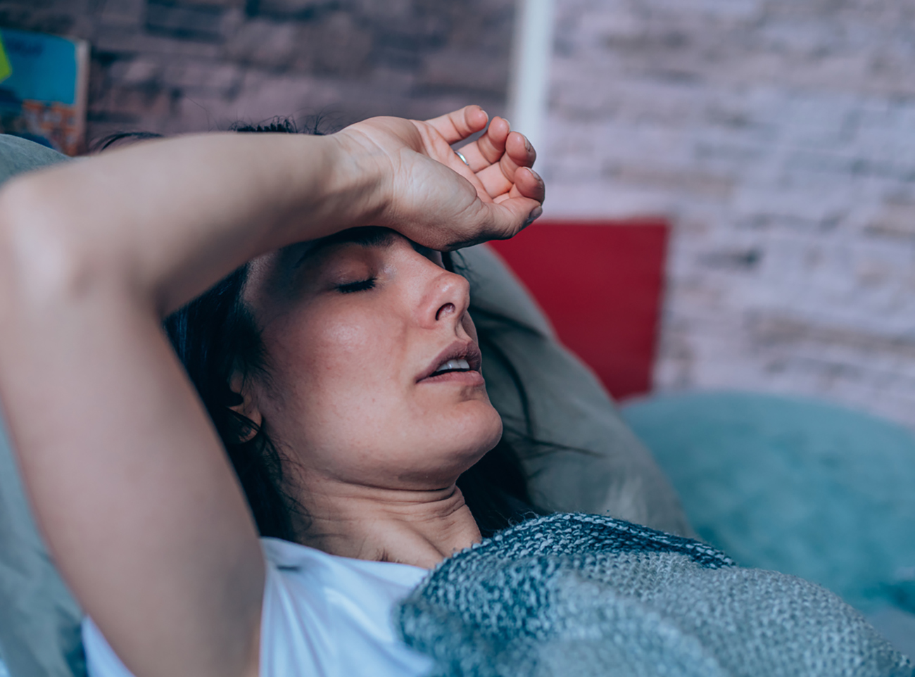 Sick young woman lying in the bed covered with blanket. Ill woman lying in bed with high temperature.