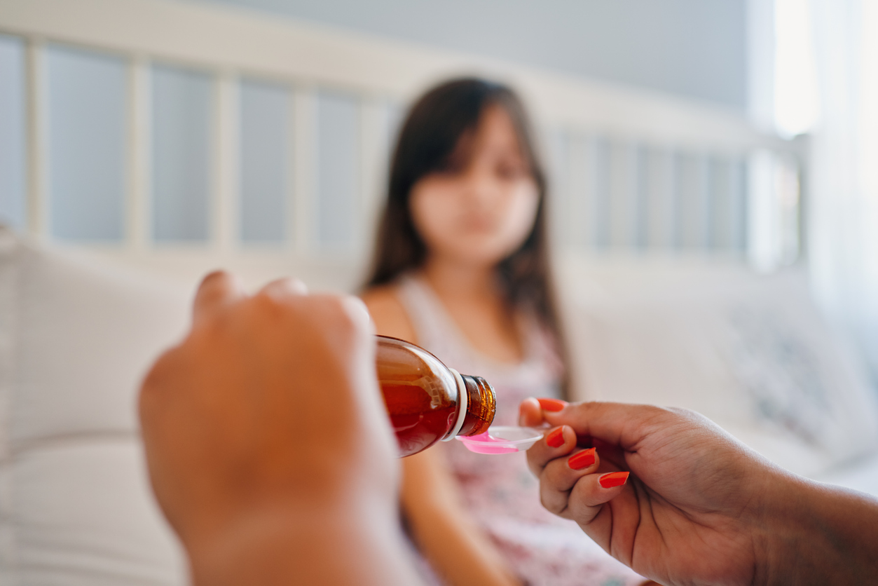 kid female waiting to eat drug. Hands of mom pouring cough syrup medicine into clear spoon to daughter
