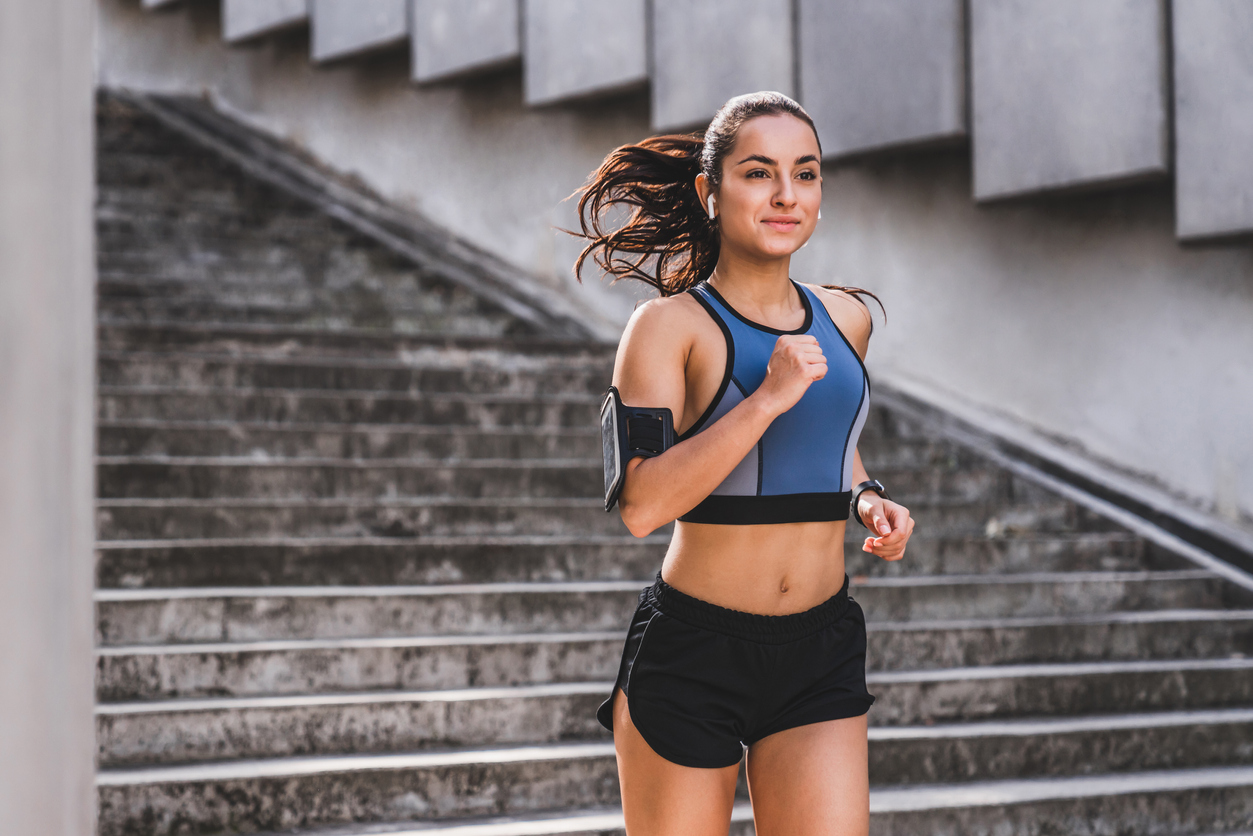 Young caucasian woman runner jogging on the stairs in sporty outfit outdoors
