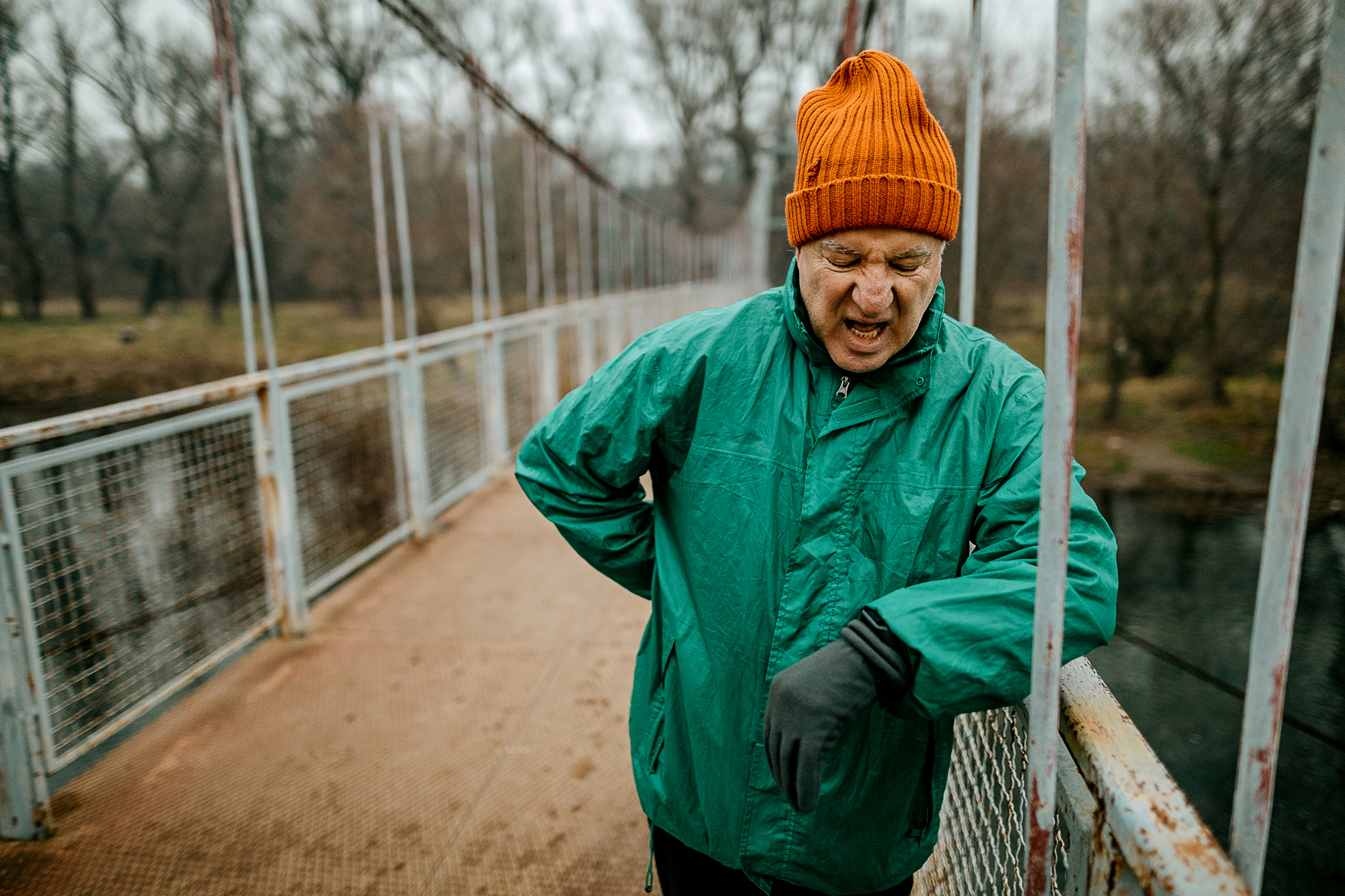 Senior man resting after jogging, he standing on a metal bridge