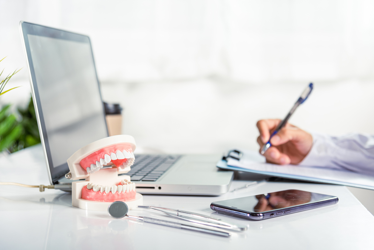 Oral dental. Dentist doctor in uniform writing information of patient in paperwork checklist on clipboard on desk office, teeth model, X-ray on laptop screen, prescription medical dental healthcare