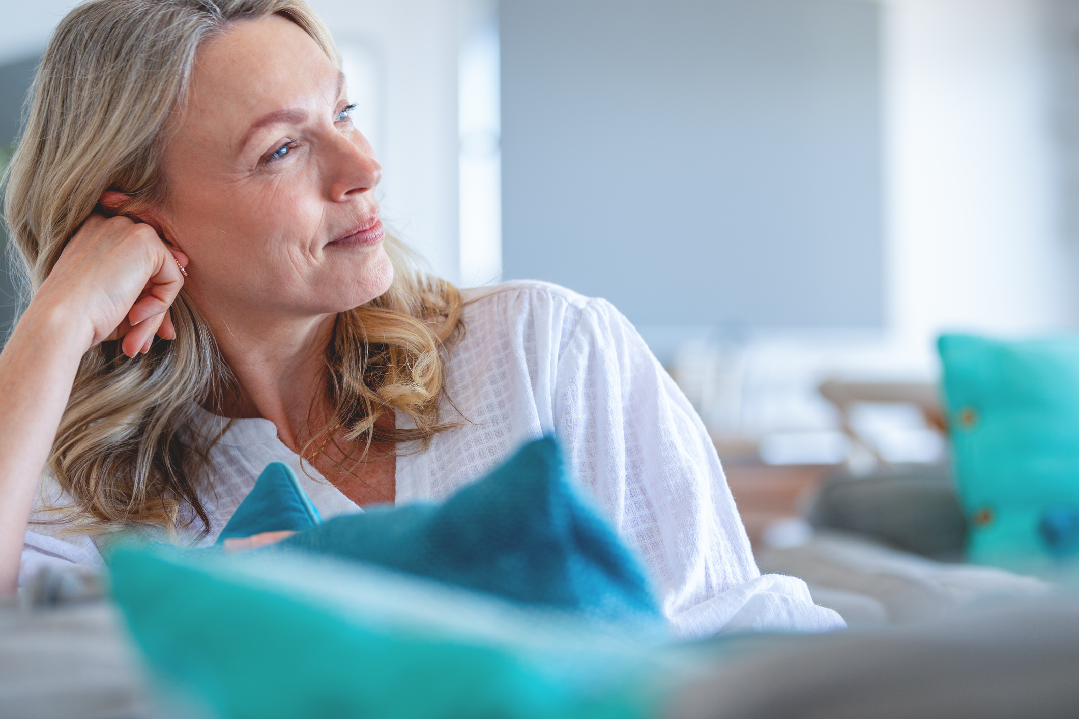 Mature woman relaxing on the sofa. She looks contented, happy and contemplative. Home can be seen in the background.