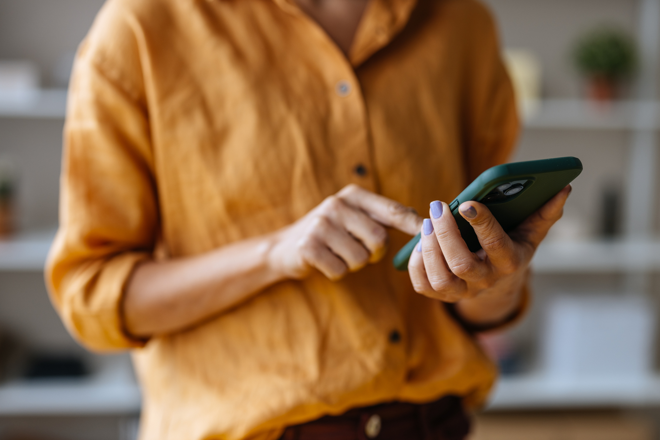 A close up view of an unrecognizable Caucasian entrepreneur texting on her smartphone while standing indoors.