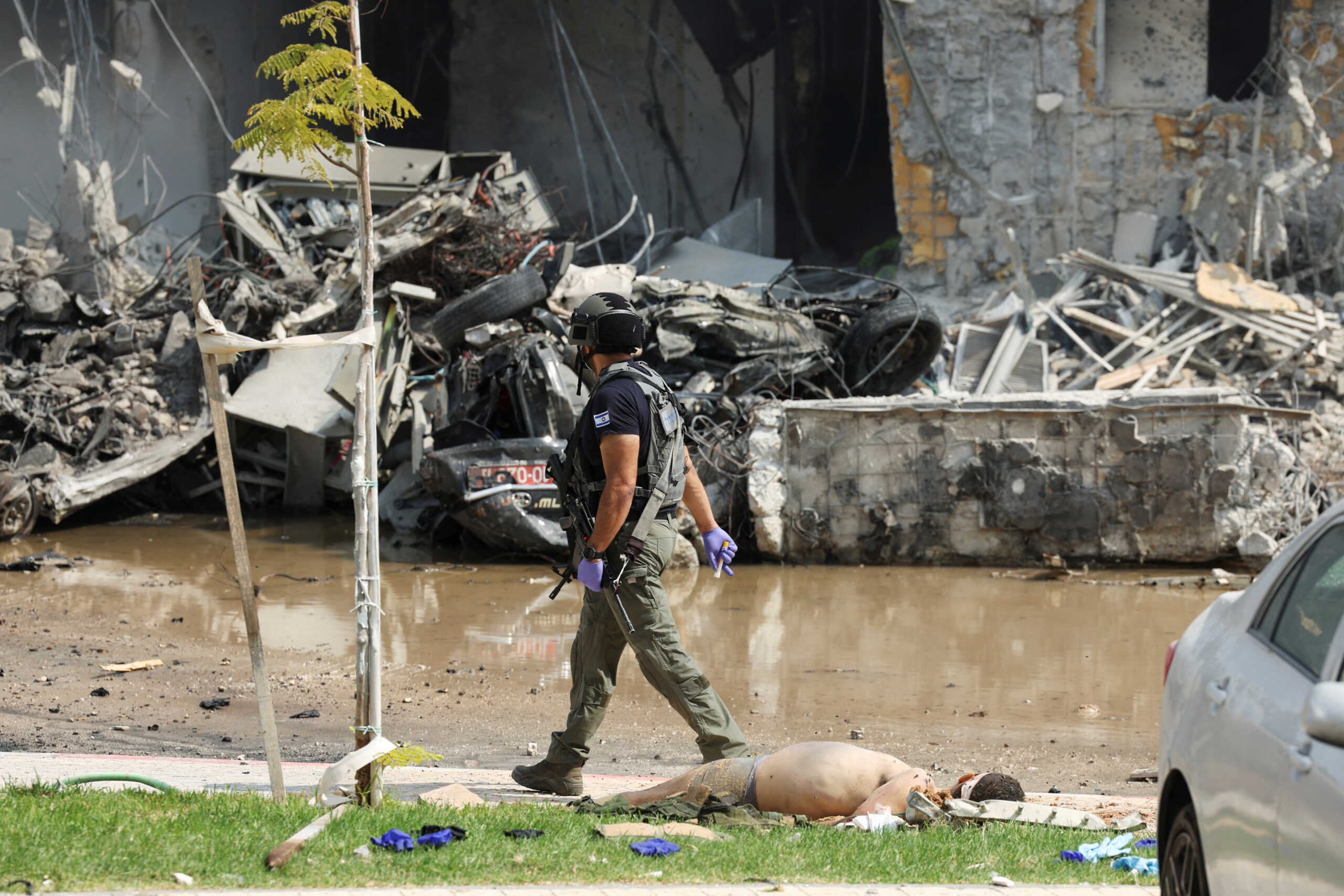 SENSITIVE MATERIAL. THIS IMAGE MAY OFFEND OR DISTURB    An Israeli security official walks past a dead body lying on grass near a destroyed police station that was the site of a battle following a mass-infiltration by Hamas gunmen from the Gaza Strip, in Sderot, southern Israel October 8, 2023. REUTERS