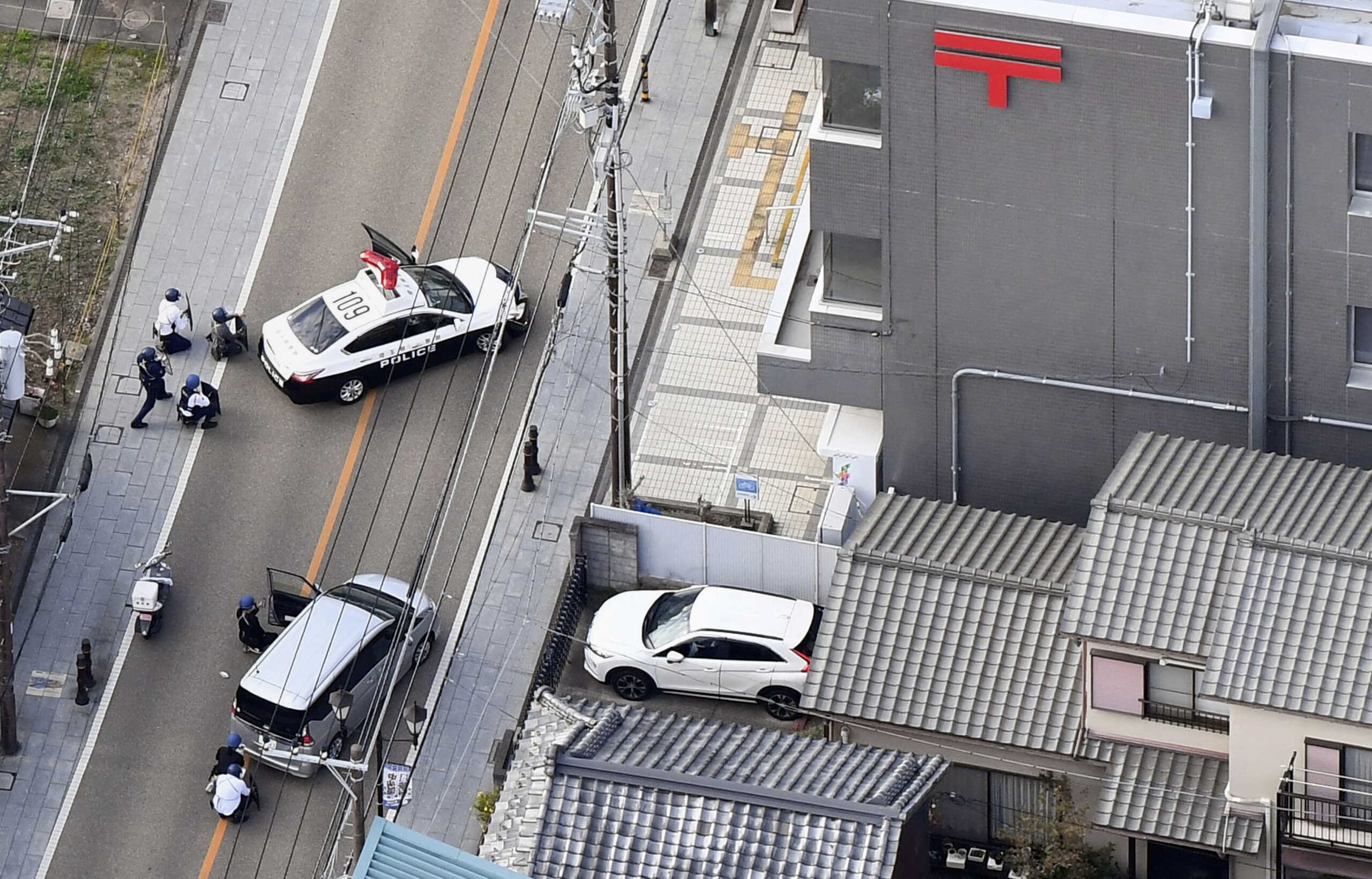 Police officers take cover behind cars outside the post office where a suspected gunman has taken people hostage after injuring two at a hospital, in Warabi, Saitama Prefecture, Japan October 31, 2023, in this photo taken by Kyodo. Mandatory credit Kyodo