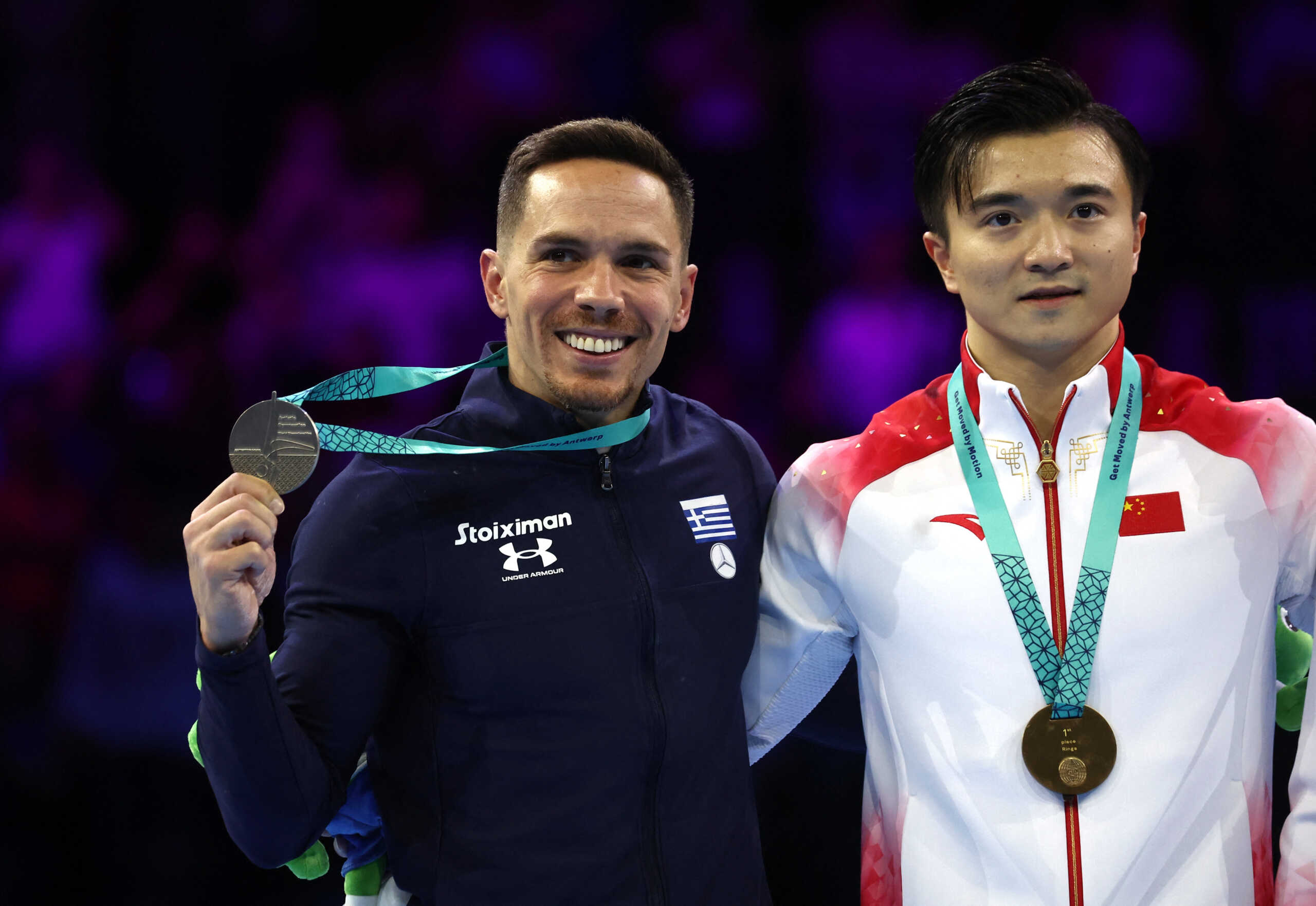Gymnastics - 2023 World Artistic Gymnastics Championships - Sportpaleis, Antwerp, Belgium - October 7, 2023 Gold medallist China's Yang Liu celebrates on the podium after winning the rings exercise at men's apparatus finals alongside silver medallist Greece's Eleftherios Petrounias REUTERS