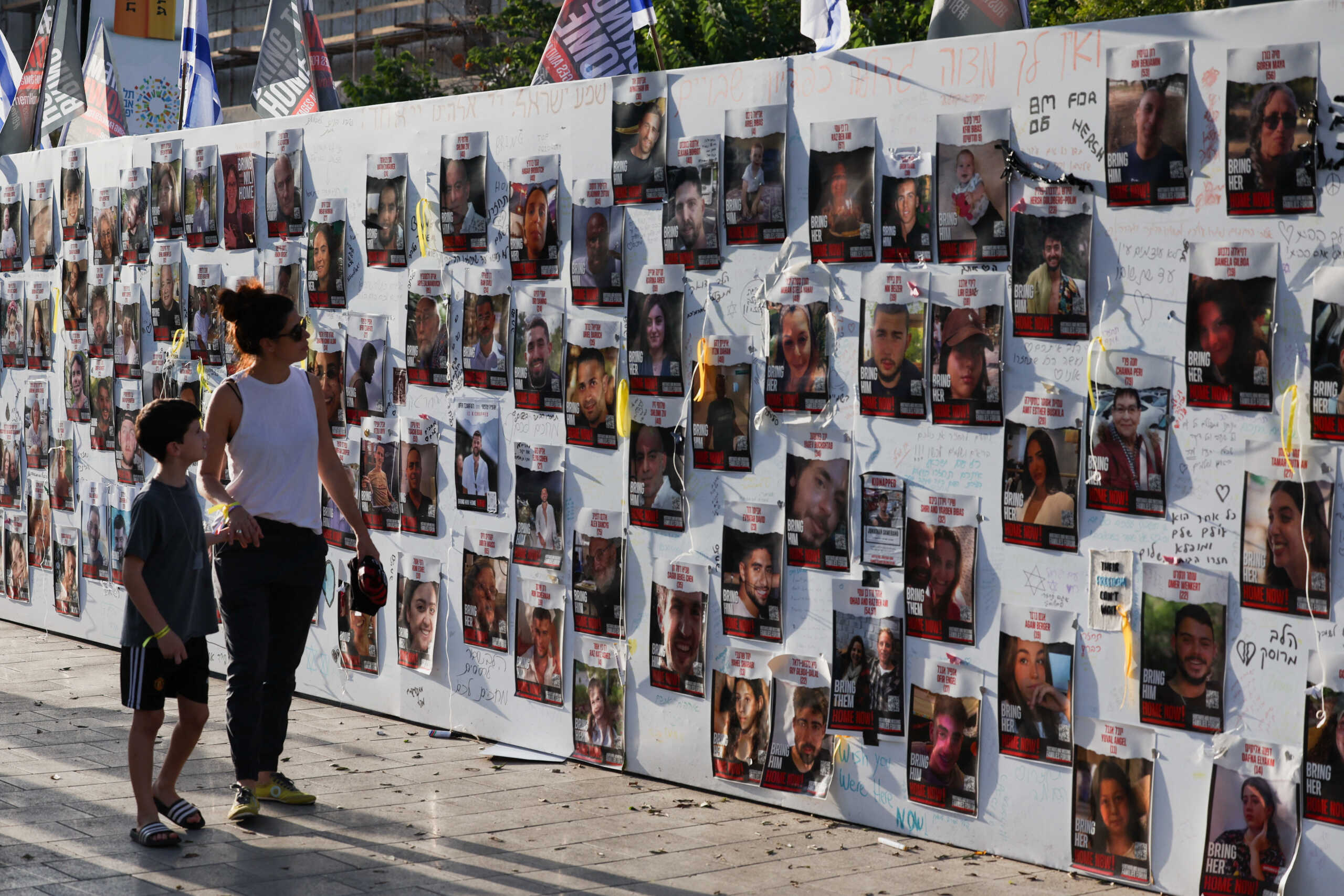 A woman with a child walks next to the wall with pictures, dedicated to hostages that are being held in Gaza after they were kidnapped from Israel by Hamas gunmen on October 7, as families and supporters of hostages hold a demonstration calling for their immediate release in Tel Aviv, Israel November 3, 2023. REUTERS