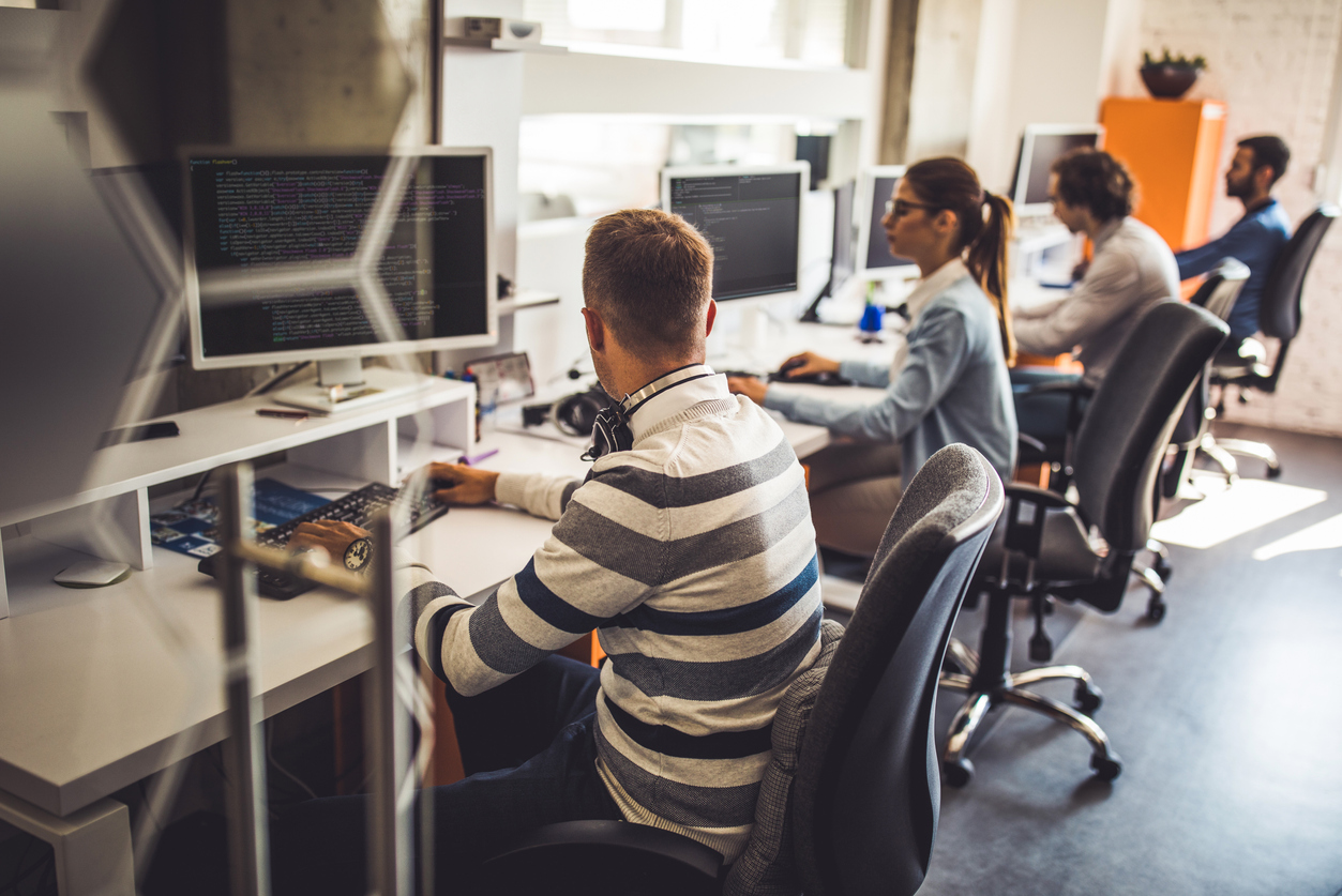 Group of programmers developing new software on desktop PC's in the office. Focus is on man in the foreground.