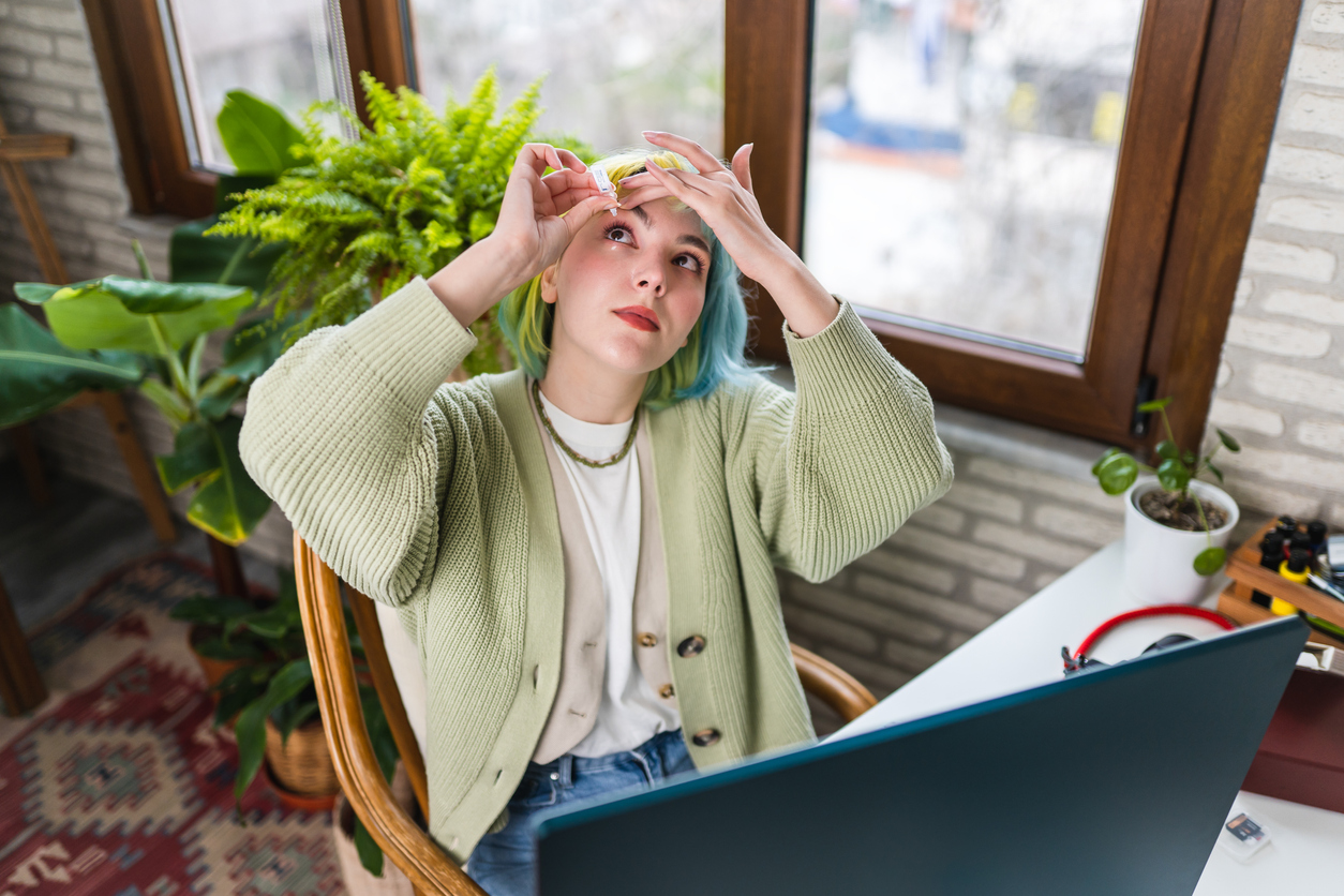 Young woman with dry eye uses eye drops while working