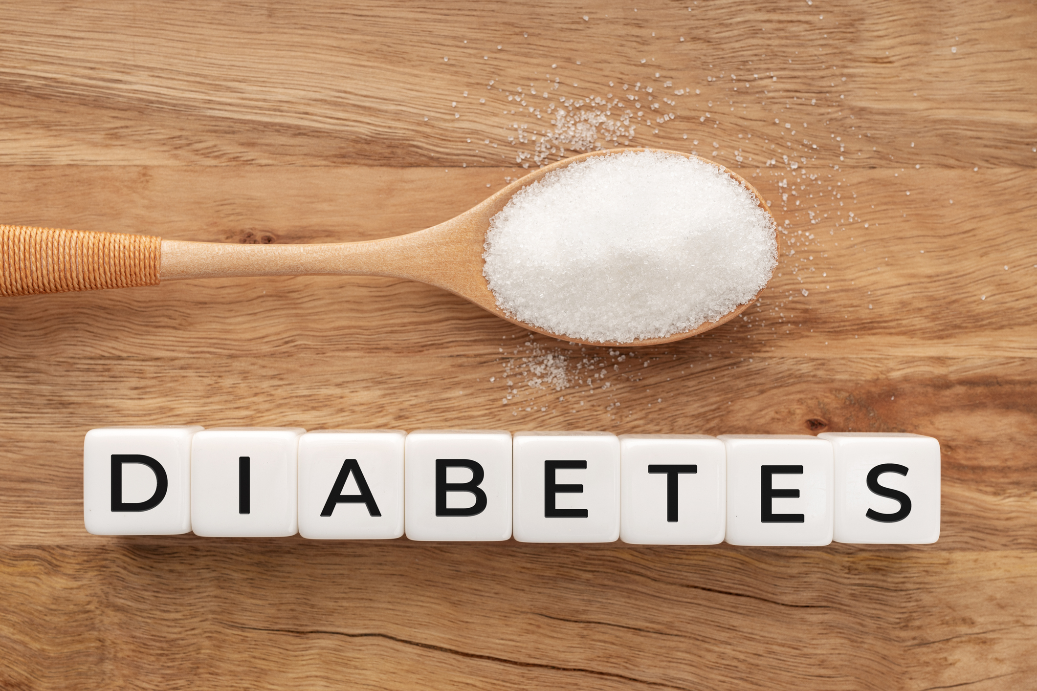 Diabetes word on bock shape and spoon with sugar inside on wooden table. Flat lay
