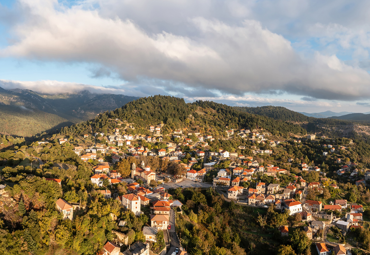 Greece, mountain village Kosmas aerial drone view, Peloponnese. Traditional tile roof and stone wall buildings, forest trees, cloudy blue sky, Autumn