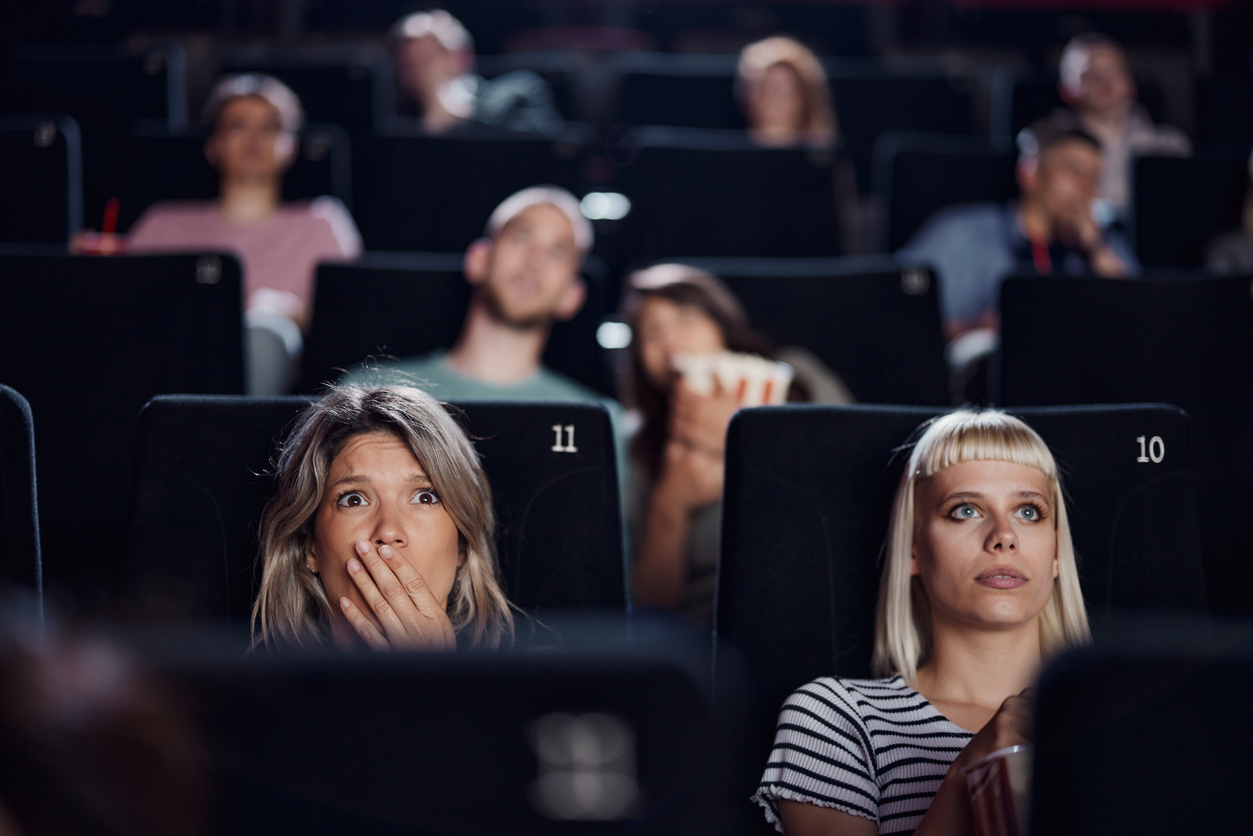Shocked woman watching a crime film in a movie theatre with other spectators.