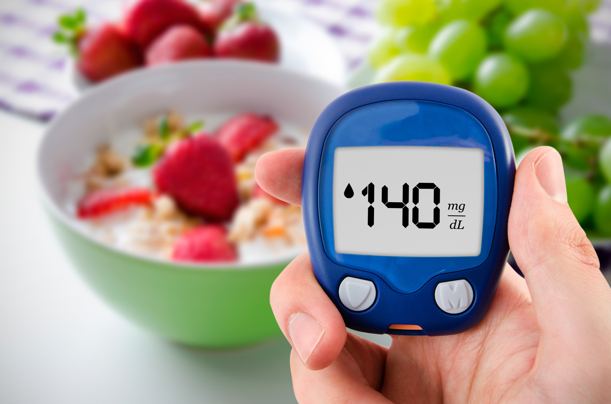 Hand holding meter. Diabetes doing glucose level test. Fruits in background