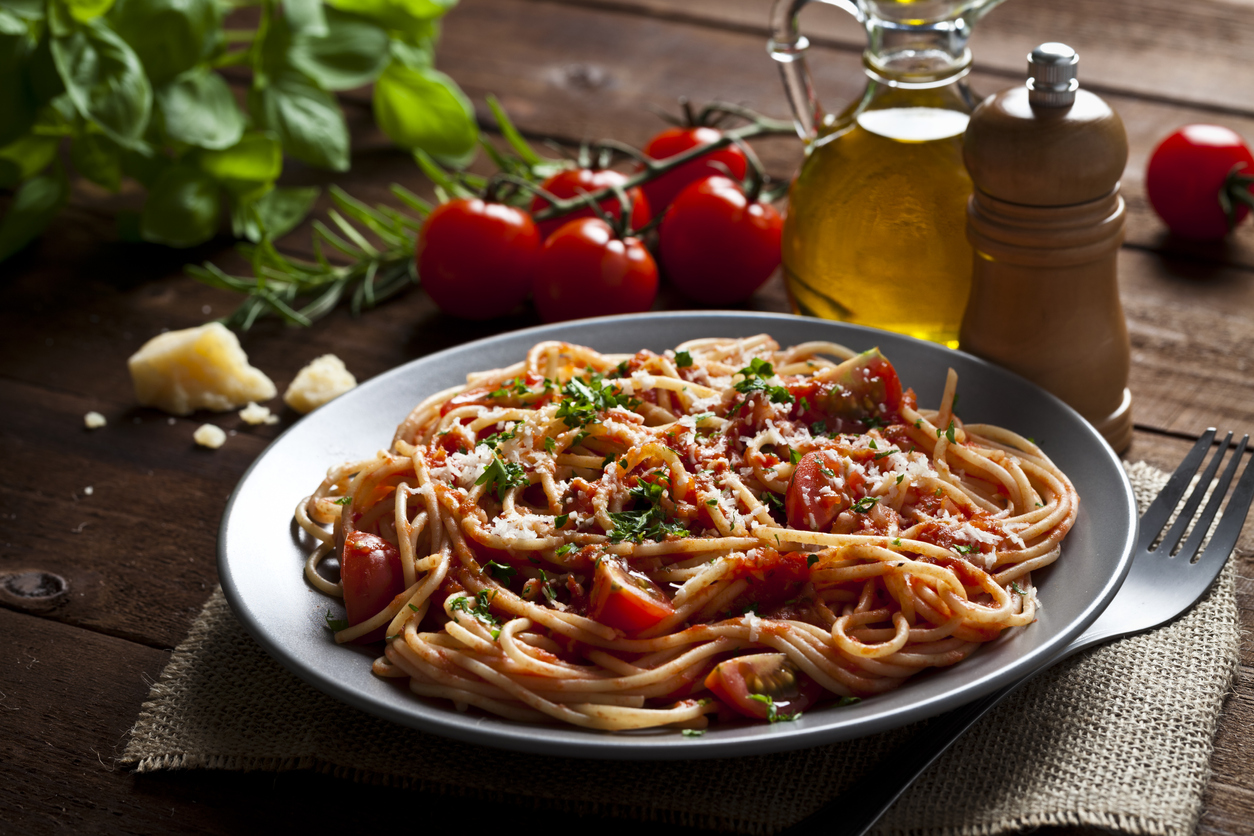 Pasta with tomato sauce shot on rustic wood table. Some ingredients for cooking pasta like tomatoes, olive oil, basil, parmesan cheese and a pepper mill are around the plate. DSRL low key studio photo taken with Canon EOS 5D Mk II and Canon EF 100mm f