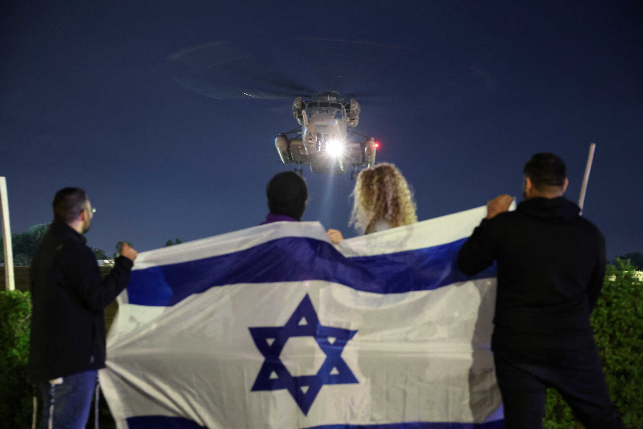 People hold an Israeli flag as a helicopter carrying hostages released amid a hostages-prisoners swap deal between Hamas and Israel arrives at Sheba Medical Center in Ramat Gan, Tel Aviv district, Israel, November 28, 2023. REUTERS