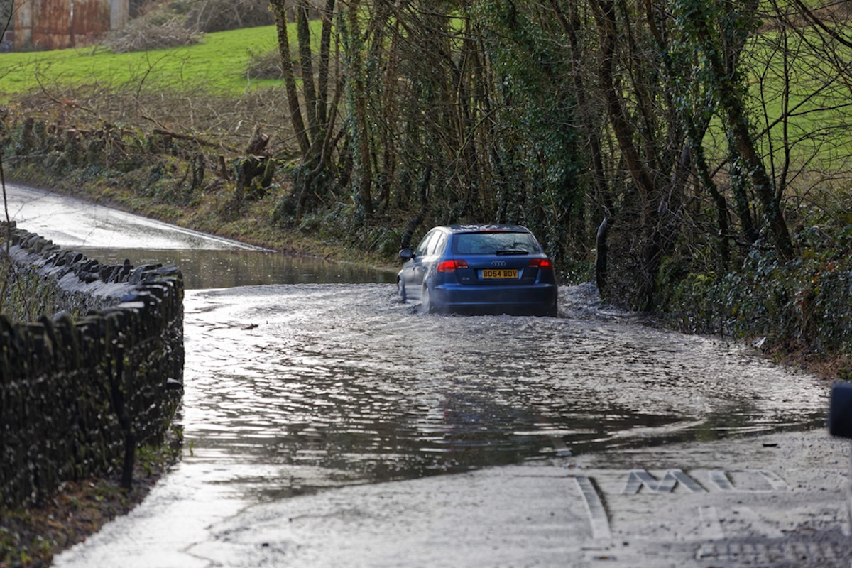 epa08223857 A car drives through a flooded road during the cleanup after storm Dennis in Crickhowell, Wales, Britain, 17 February 2020. Storm Dennis hit the region over the past weekend bringing torrential rains, floods and landslides.  EPA