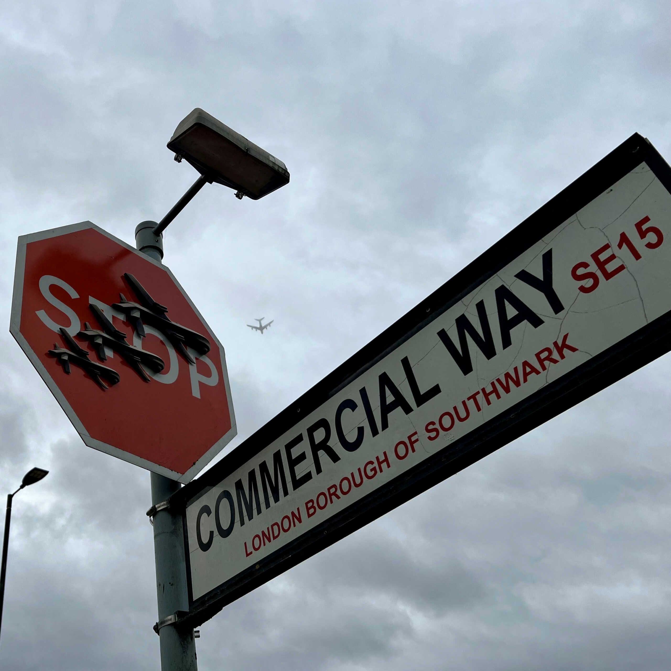 Airplane passes overhead as Banksy artwork depicting drones covers a stop sign in London, Britain December 22, 2023 in this picture obtained from social media. Joe Brown via REUTERS  THIS IMAGE HAS BEEN SUPPLIED BY A THIRD PARTY. MANDATORY CREDIT. NO RESALES. NO ARCHIVES.