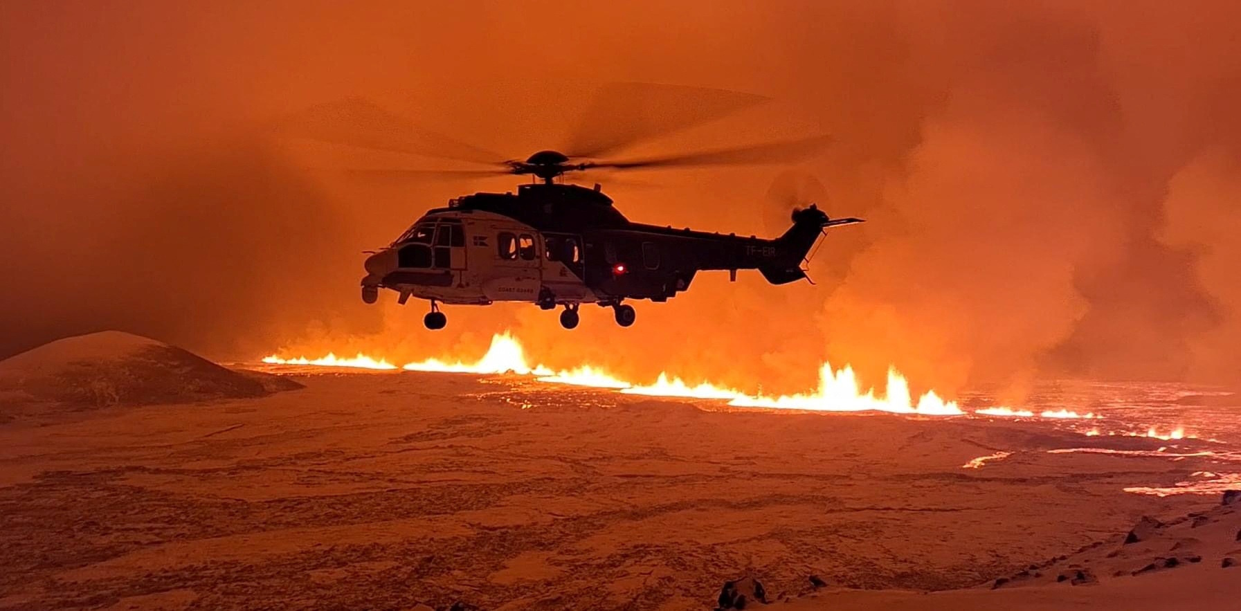 A helicopter flies near a volcano spewing lava and smoke as it erupts near Grindavik, Iceland, December 19, 2023. Icelandic Coast Guard