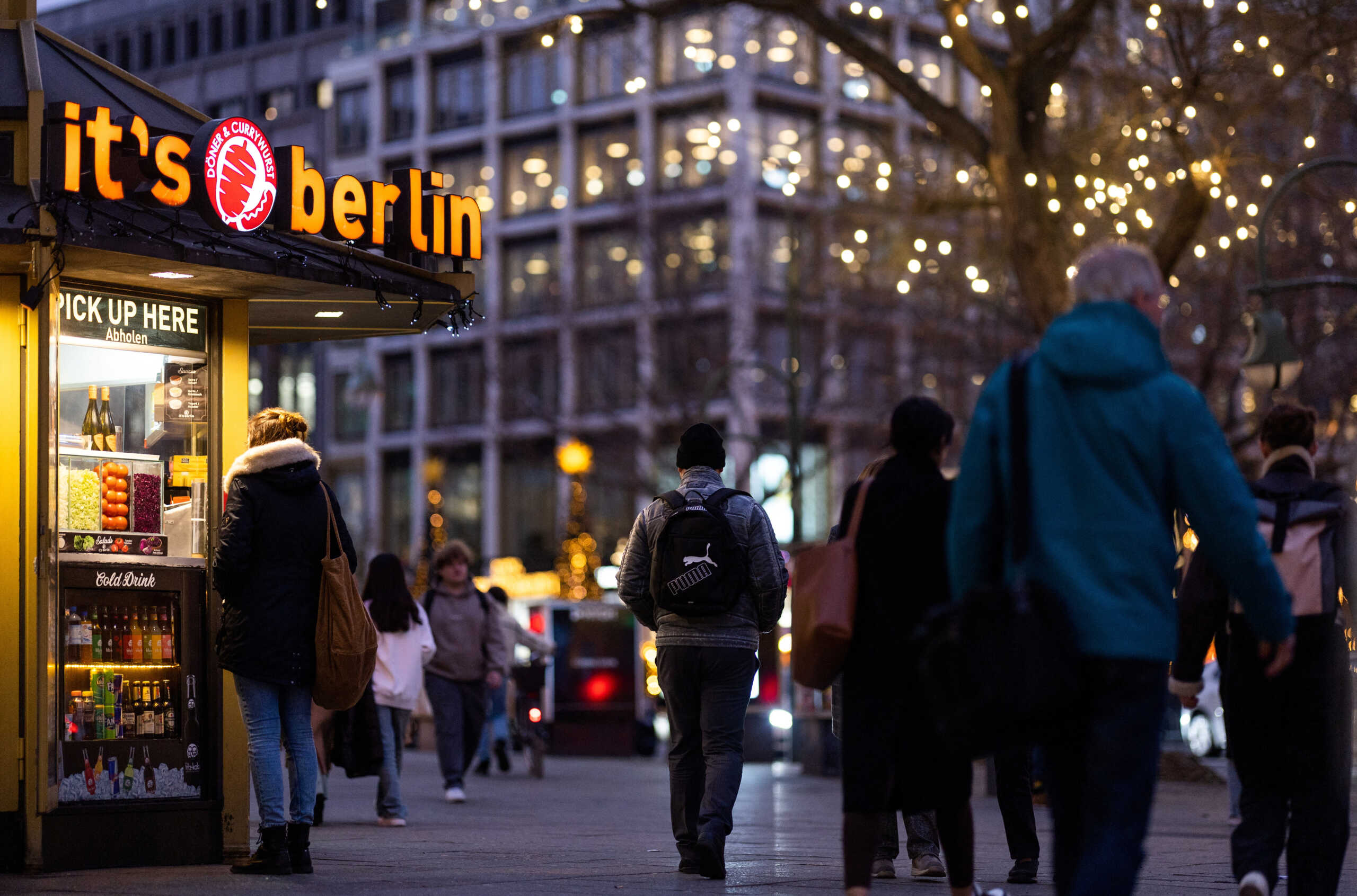 People walk next to a Doner kebab and Currywurst booth at Kurfuerstendamm shopping street during Christmas season in Berlin, Germany, December 18, 2023.  REUTERS