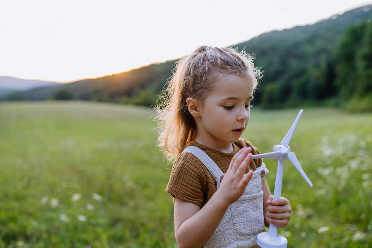 Little girl standing in nature with model of wind turbine. Concept of ecology future and renewable resources.