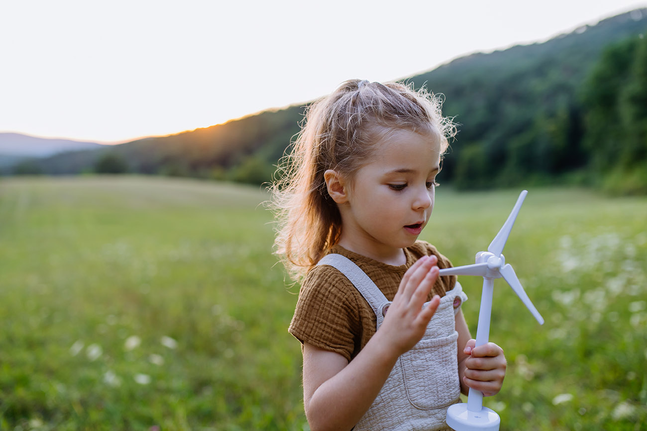 Little girl standing in nature with model of wind turbine. Concept of ecology future and renewable resources.