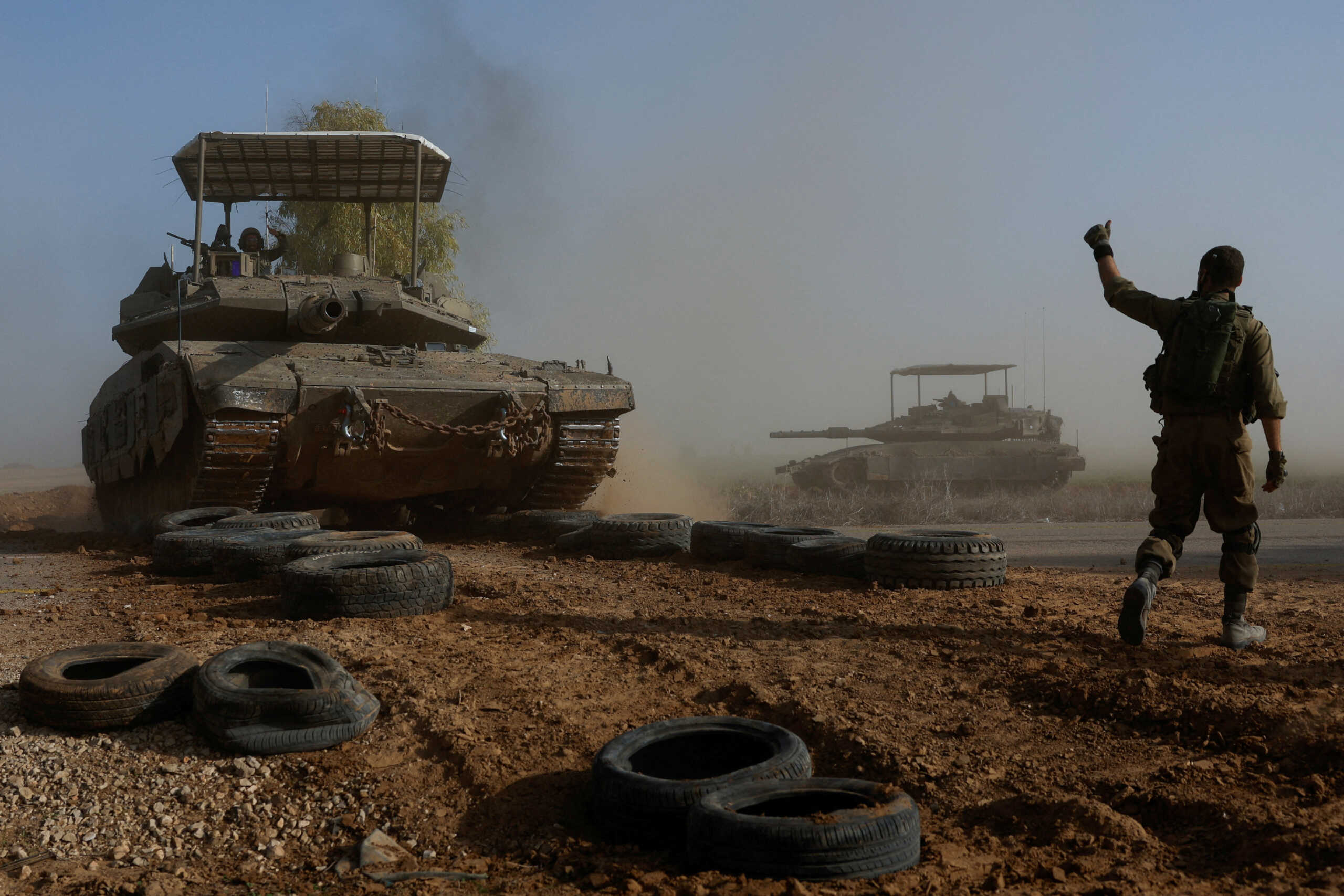 An Israeli soldier gestures towards a tank crew member as it crosses a road, as part of the convoy, amid the ongoing conflict between Israel and the Palestinian Islamist group Hamas, near Israel's border with southern Gaza, in Israel, December 4, 2023. REUTERS