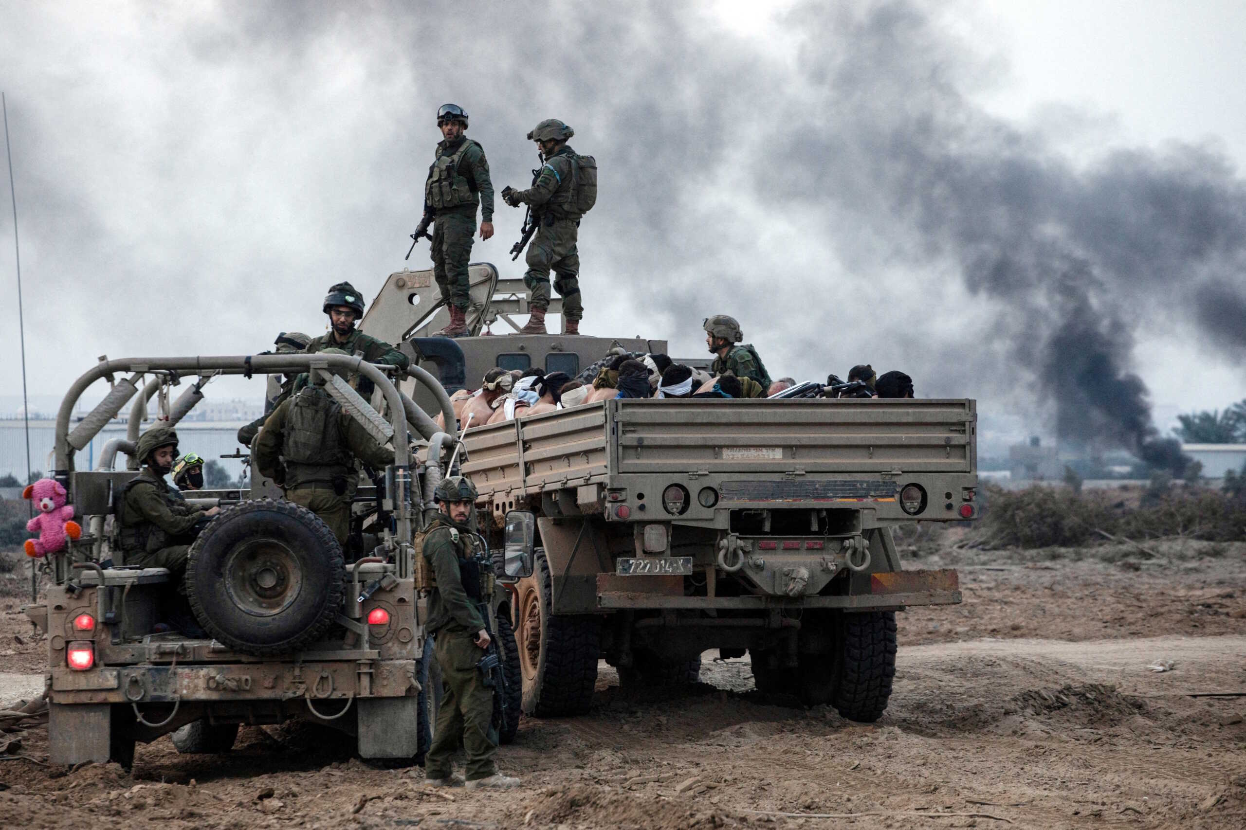 Palestinian detainees sit in a truck as Israeli soldiers guard around amid the ongoing conflict between Israel and the Palestinian Islamist group Hamas, in the Gaza Strip December 8, 2023.  REUTERS