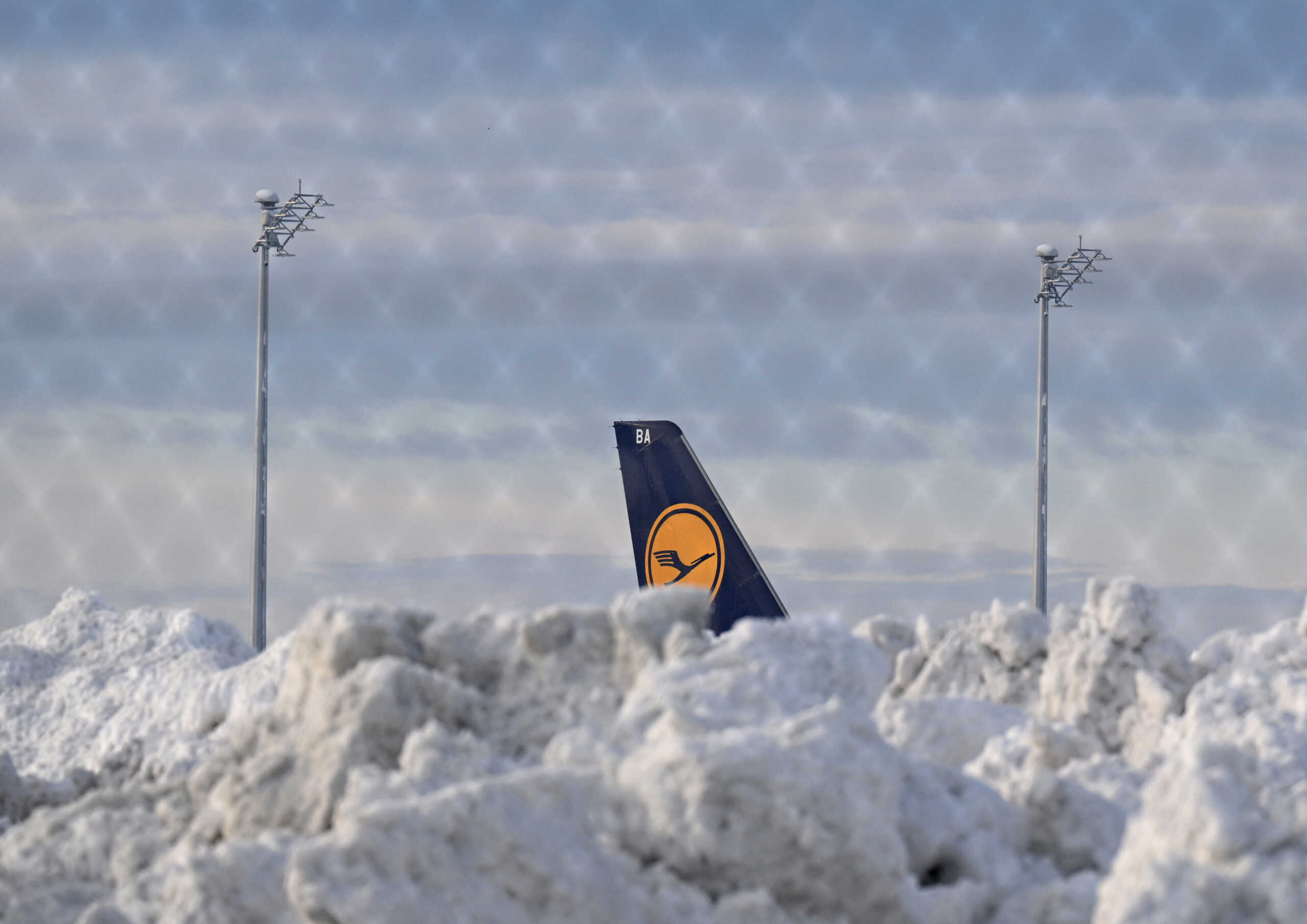 A tail fin of a Lufthansa plane is pictures behind snow at the terminal as Munich Airport has cancelled all incoming and outgoing flights until 12 p.m. (1100GMT) due to a forecast for sleet in Munich, Germany, December 5, 2023. Picture taken through a fence.     REUTERS