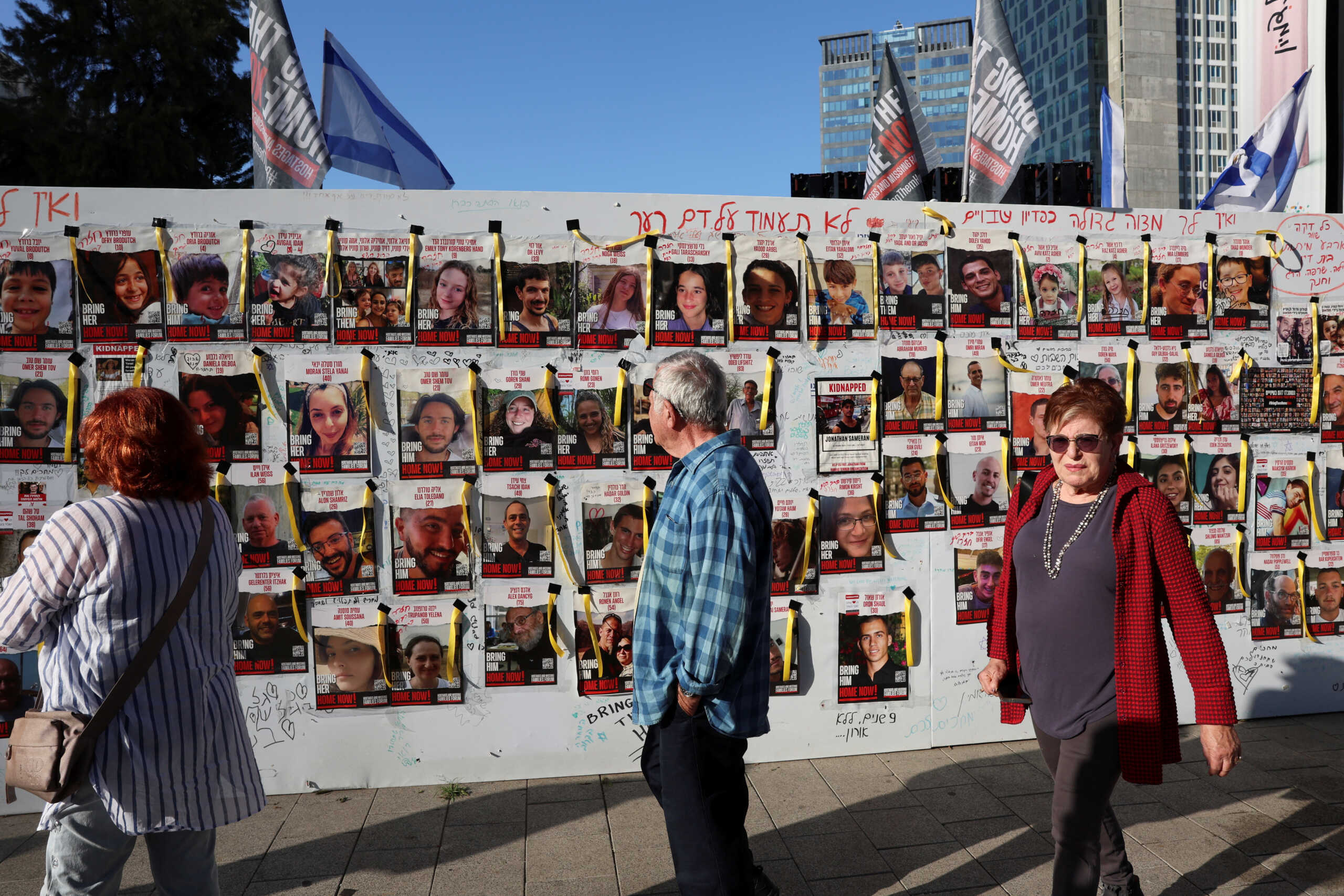 People walk past a wall with posters depicting missing people, on the day of a a demonstration called by mothers of hostages kidnapped on the deadly October 7 attack by Palestinian Islamist group Hamas, amid a temporary truce, in Tel Aviv, Israel, November 30, 2023. REUTERS