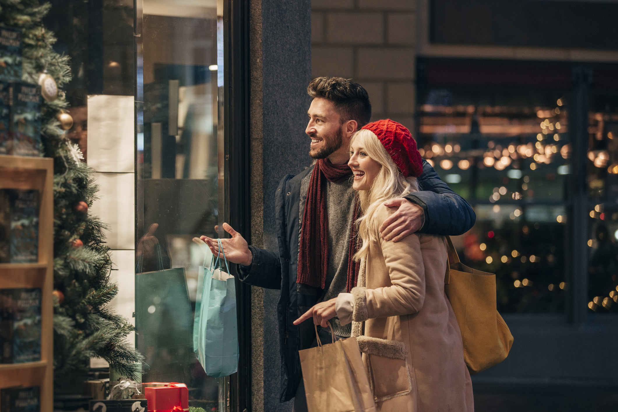 Side view of a couple doing some window shopping at christmas. The mid adult male has his arm around the mid adult female and they are talking about wats in the window.
