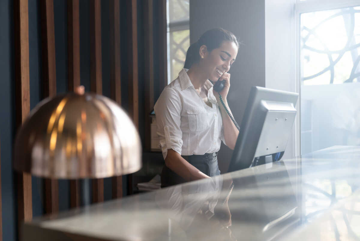 Beautiful friendly hotel receptionist answering a call from a guest smiling very happy